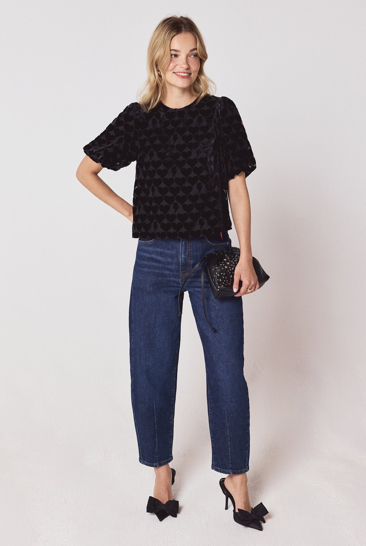 Scamp & Dude Black Heart & Bolt Burn Out Velvet Tie Back Blouse | Model wearing a black heart and bolt burn out top with a pair of dark blue barrel jeans and black bow heels.