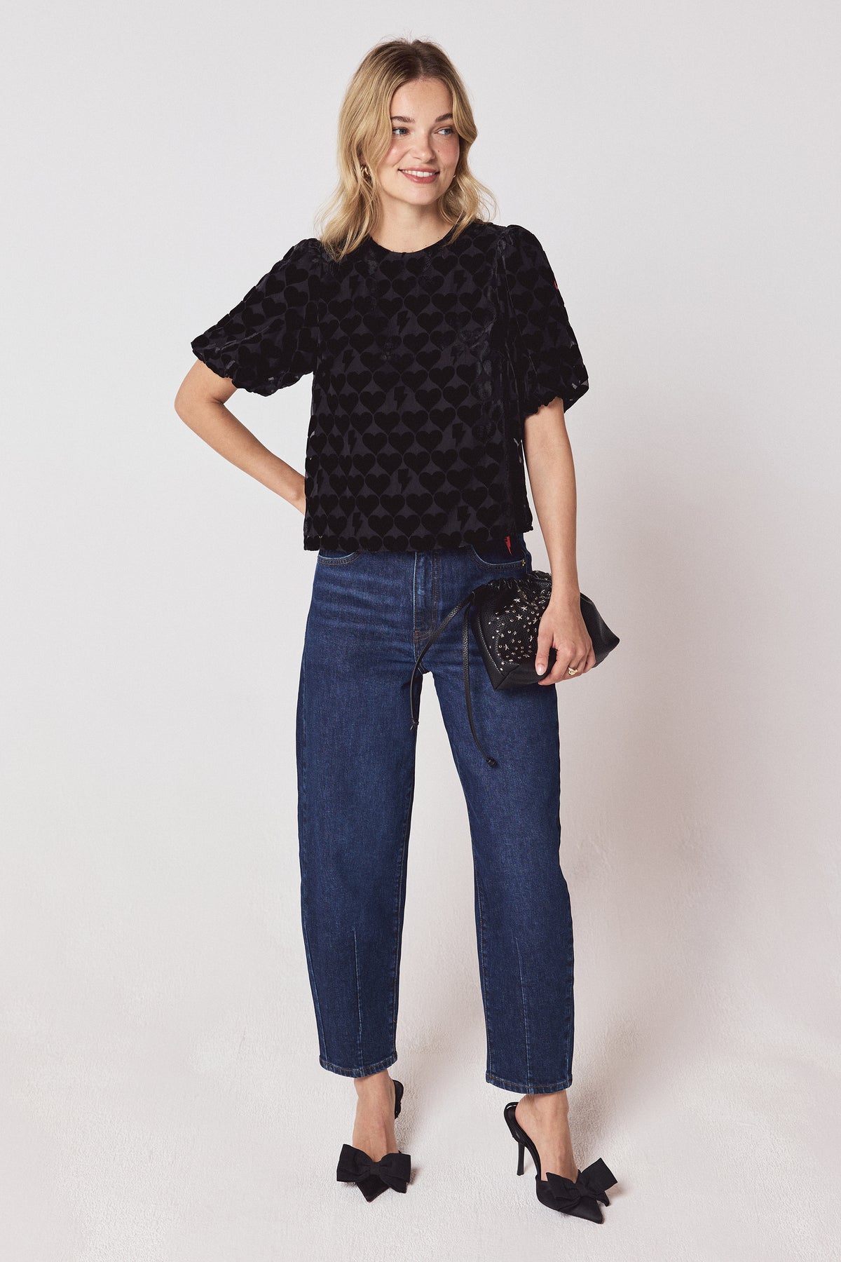 Scamp & Dude Black Heart & Bolt Burn Out Velvet Tie Back Blouse | Model wearing a black heart and bolt burn out top with a pair of dark blue barrel jeans and black bow heels.
