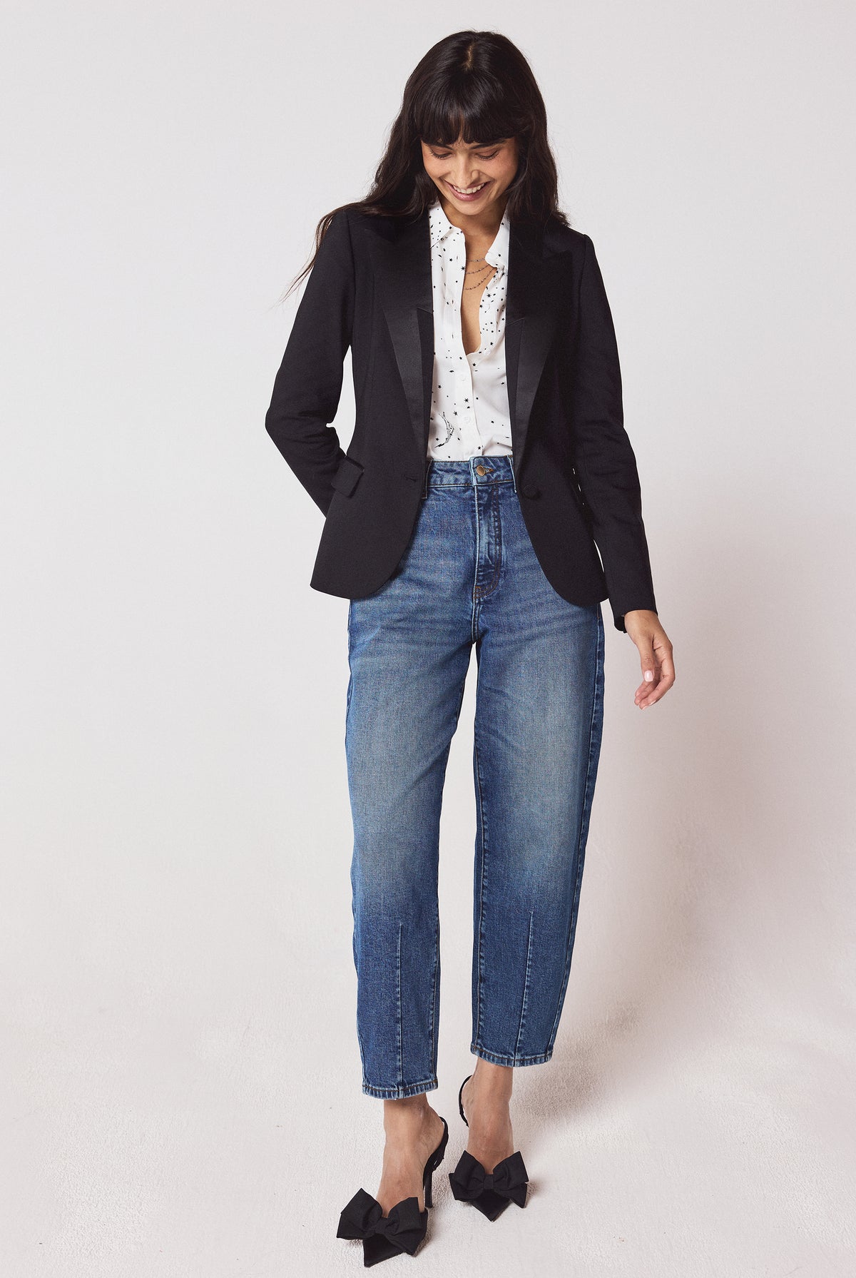 Scamp & Dude Black Ultimate Tux Jacket | Model wearing a black tux jacket with a white star print shirt and blue jeans. Worn with black bow high heels.