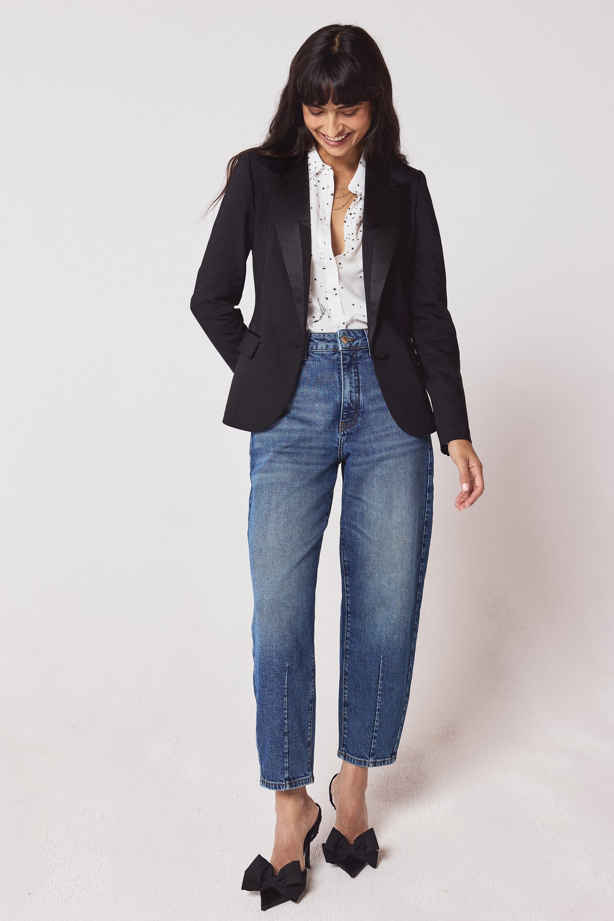 Scamp & Dude Black Ultimate Tux Jacket | Model wearing a black tux jacket with a white star print shirt and blue jeans. Worn with black bow high heels.