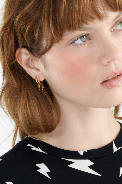 Scamp & Dude x Rachel Jackson Gold Plated Huggie Hoops with Black Pavé Detailed Lightning Bolt & Star Charms | Model with orange hair wearing gold hoop earrings with star charms
