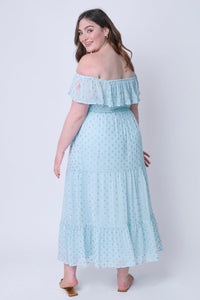 A brunette lady wearing a light blue with gold lurex spots Bardot midi dress off the shoulder with gold sandals