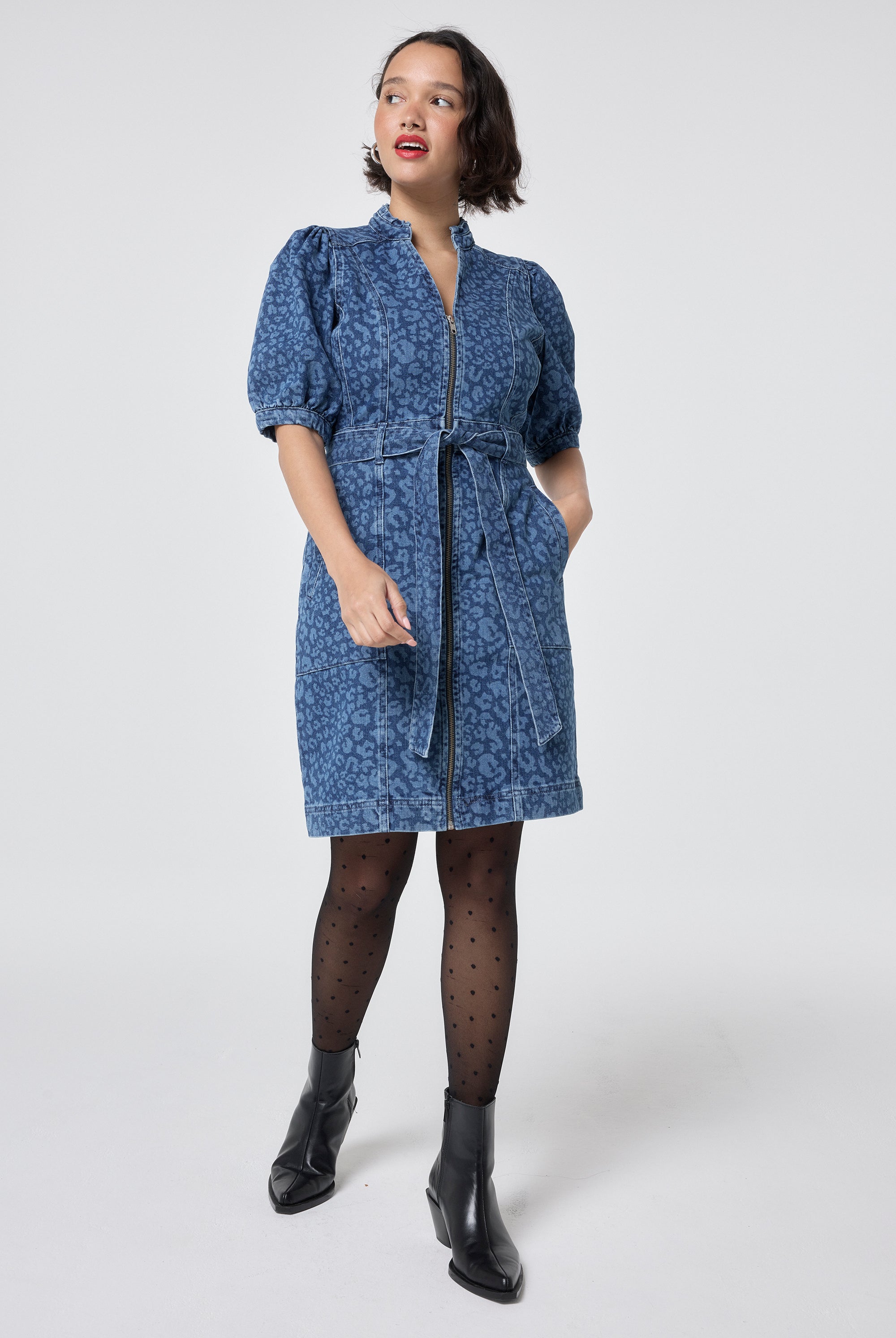 Scamp and Dude Authentic Indigo Leopard Zip Detail Short Denim Dress | Model wearing a denim leopard print short dress with a tie waist detail, paired with tights and black boots.