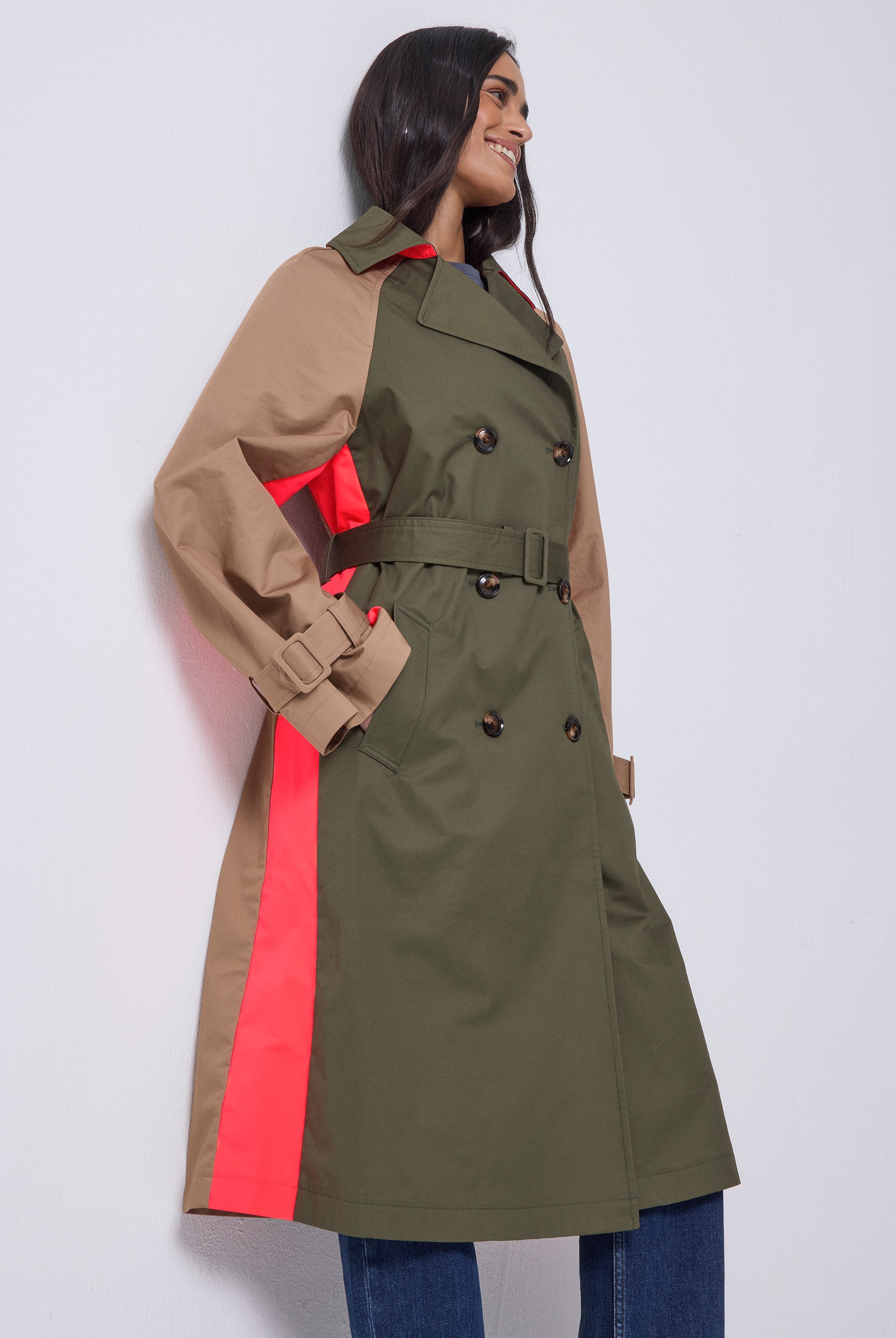 Scamp and Dude Khaki with Camel and Coral Colour Block Trench Coat | Model wearing a khaki trench coat that has camel sleeves and a coral stripe. Paired with blue jeans and heeled boots.