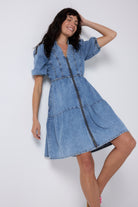 Scamp and Dude Pale Indigo Zip Detail Tiered Short Denim Dress | Model wearing a short pale blue denim dress with zip front and tiered detail. Worn with pink trainers.