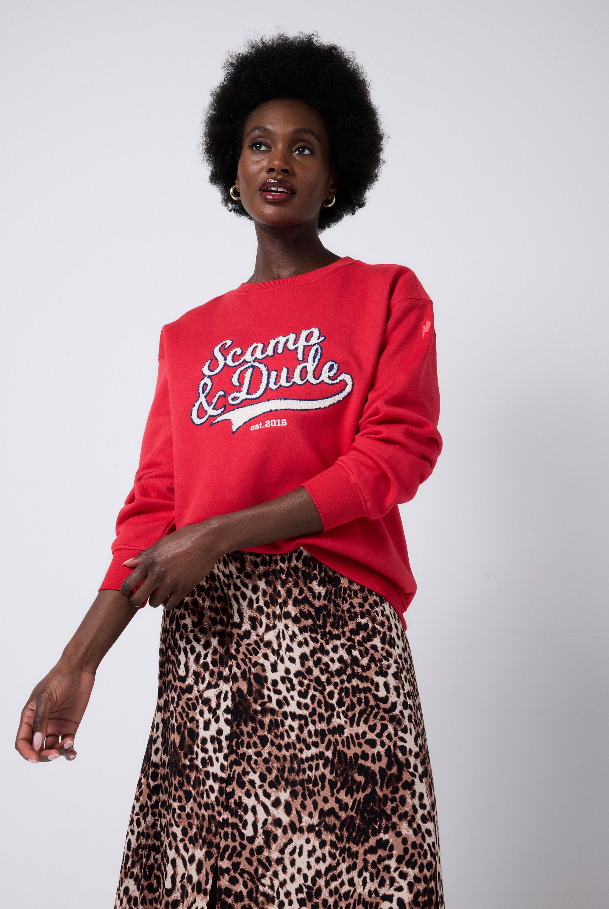 Scamp and Dude Red Varsity Scamp & Dude Oversized Sweatshirt | Model wearing a neutral cheetah print skirt with an oversized red crew neck sweatshirt with Scamp & Dude logo.