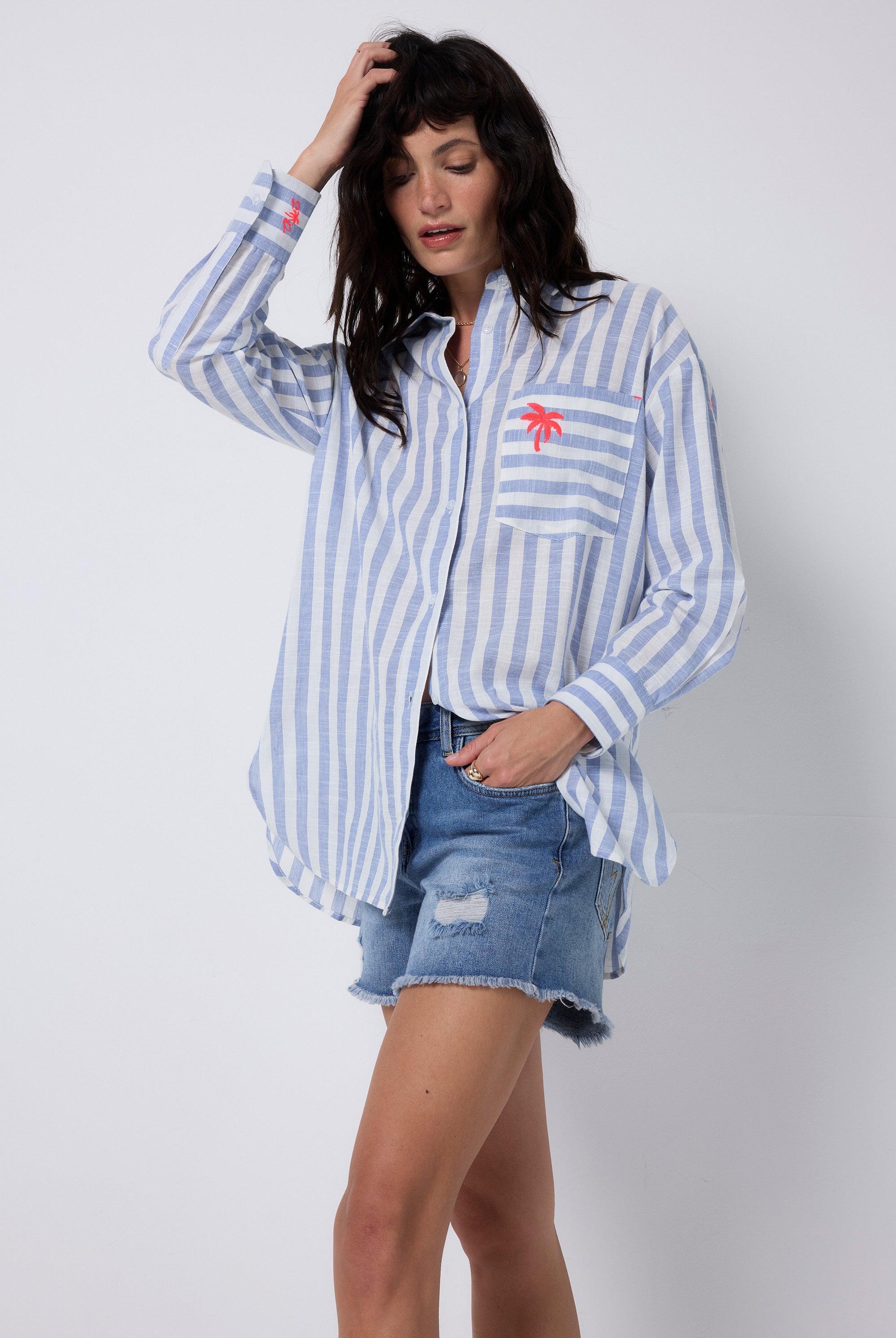 Scamp and Dude Blue and White Stripe Oversized Shirt | Model wearing a long sleeve stripe shirt that has embroidered palm tree detail. Worn with distressed denim shorts.