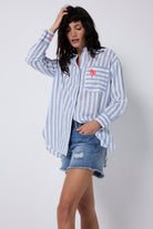 Scamp and Dude Blue and White Stripe Oversized Shirt | Model wearing a long sleeve stripe shirt that has embroidered palm tree detail. Worn with distressed denim shorts.