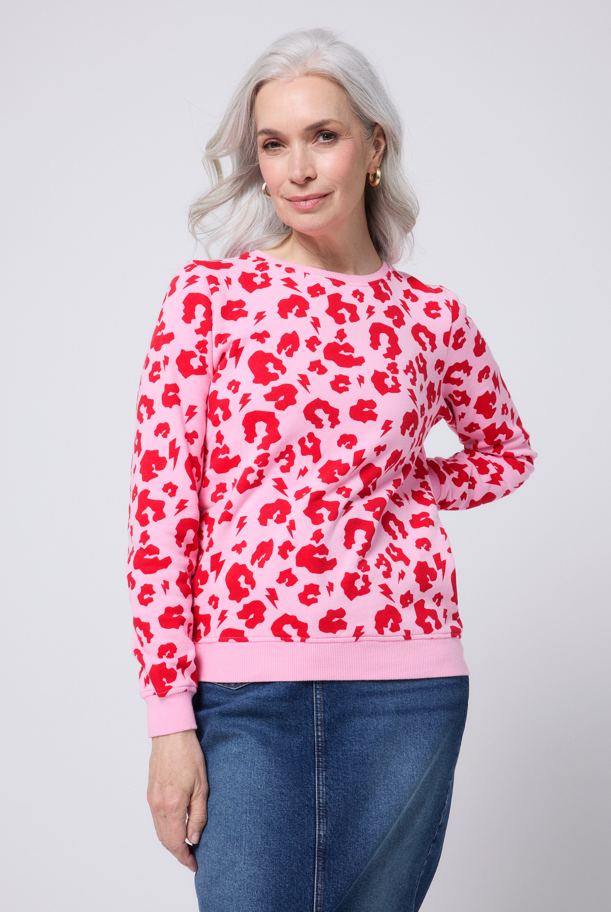 Scamp and Dude Pink with Red Leopard Sweatshirt | Model wearing a blue denim skirt with a pink crew neck sweatshirt featuring red leopard print.