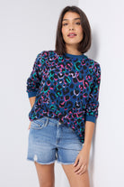 Scamp and Dude Teal with Rainbow Shadow Leopard Oversized Sweatshirt | Model wearing a pair of distressed denim shorts with a teal round neck sweatshirt featuring rainbow shadow leopard print.