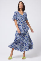 Scamp and Dude White with Blue Floral Animal Print Ruffle Detail Maxi Dress | Model wearing a white v-neck maxi dress with blue and black floral animal print. Worn with neon yellow heels.
