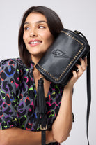 Scamp and Dude Black Twin Compartment Cross Body Bag | Model wearing a short grey zip front dress with rainbow leopard print, holding a black cross body bag with gold studs.