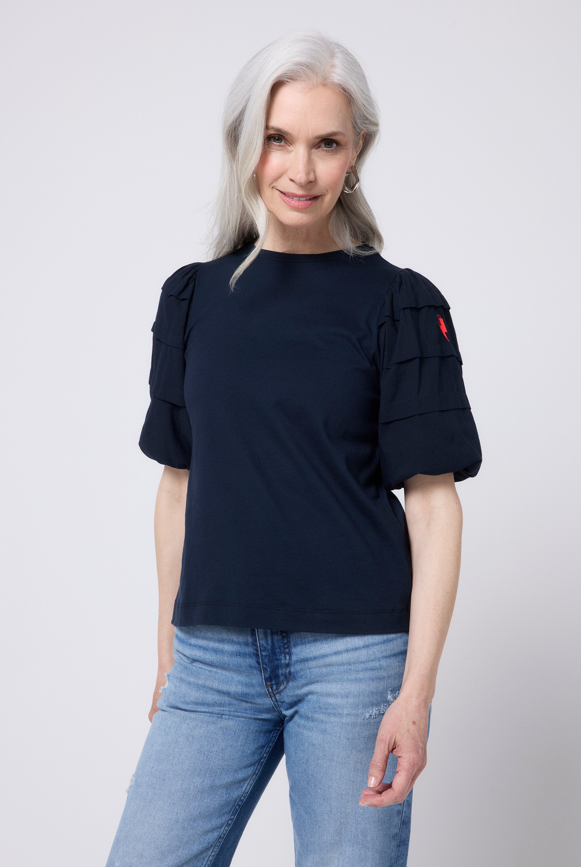 Scamp and Dude Navy Pintuck Sleeve T-Shirt | Model wearing indigo jeans with a navy pintuck sleeve t shirt and black sandals.