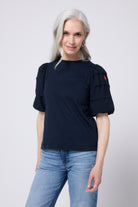 Scamp and Dude Navy Pintuck Sleeve T-Shirt | Model wearing indigo jeans with a navy pintuck sleeve t shirt and black sandals.