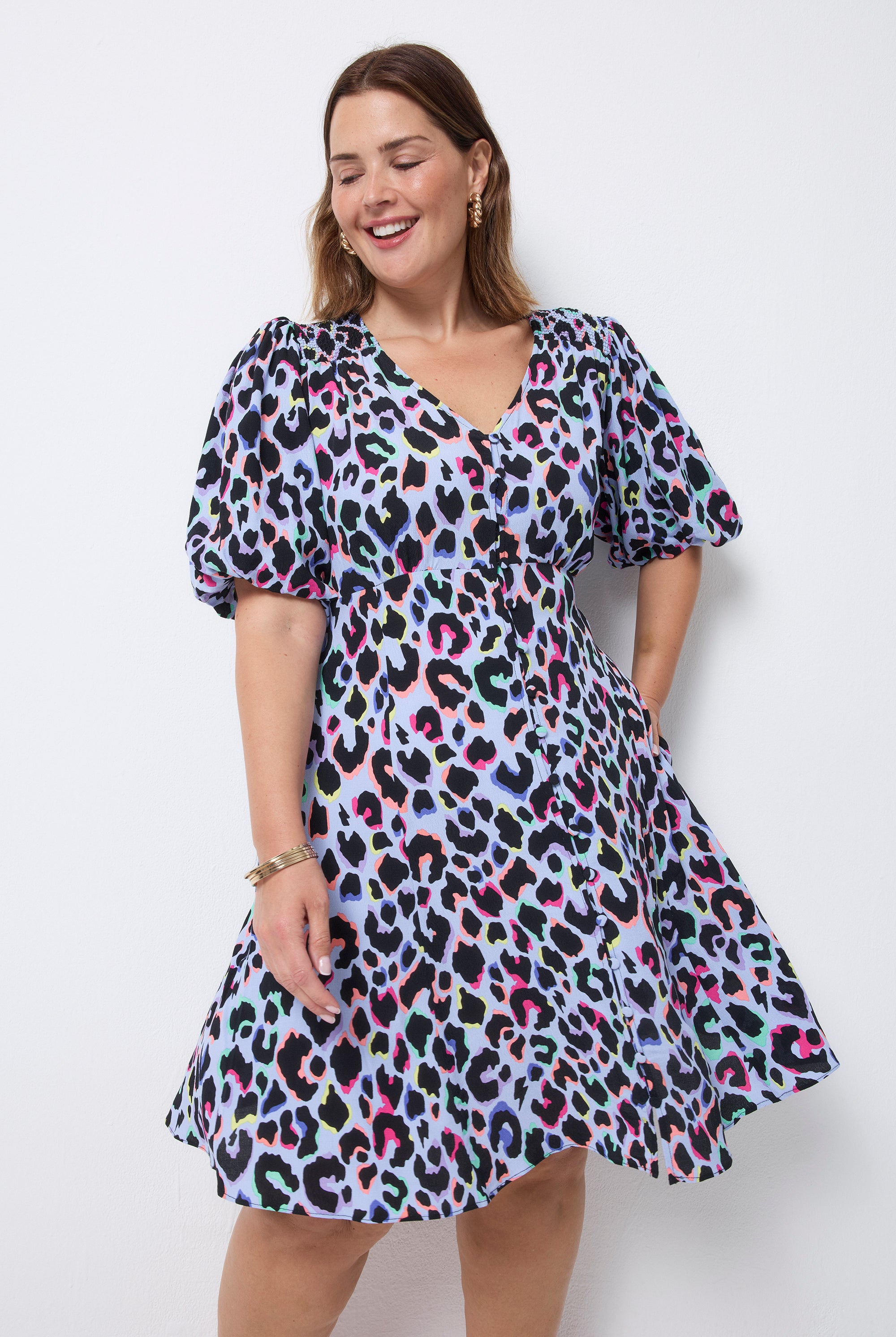 Scamp and Dude Light Blue with Rainbow Shadow Leopard Short Tea Dress | Model wearing light blue v neck short tea dress with puff sleeves and rainbow leopard print. Paired with sandals.