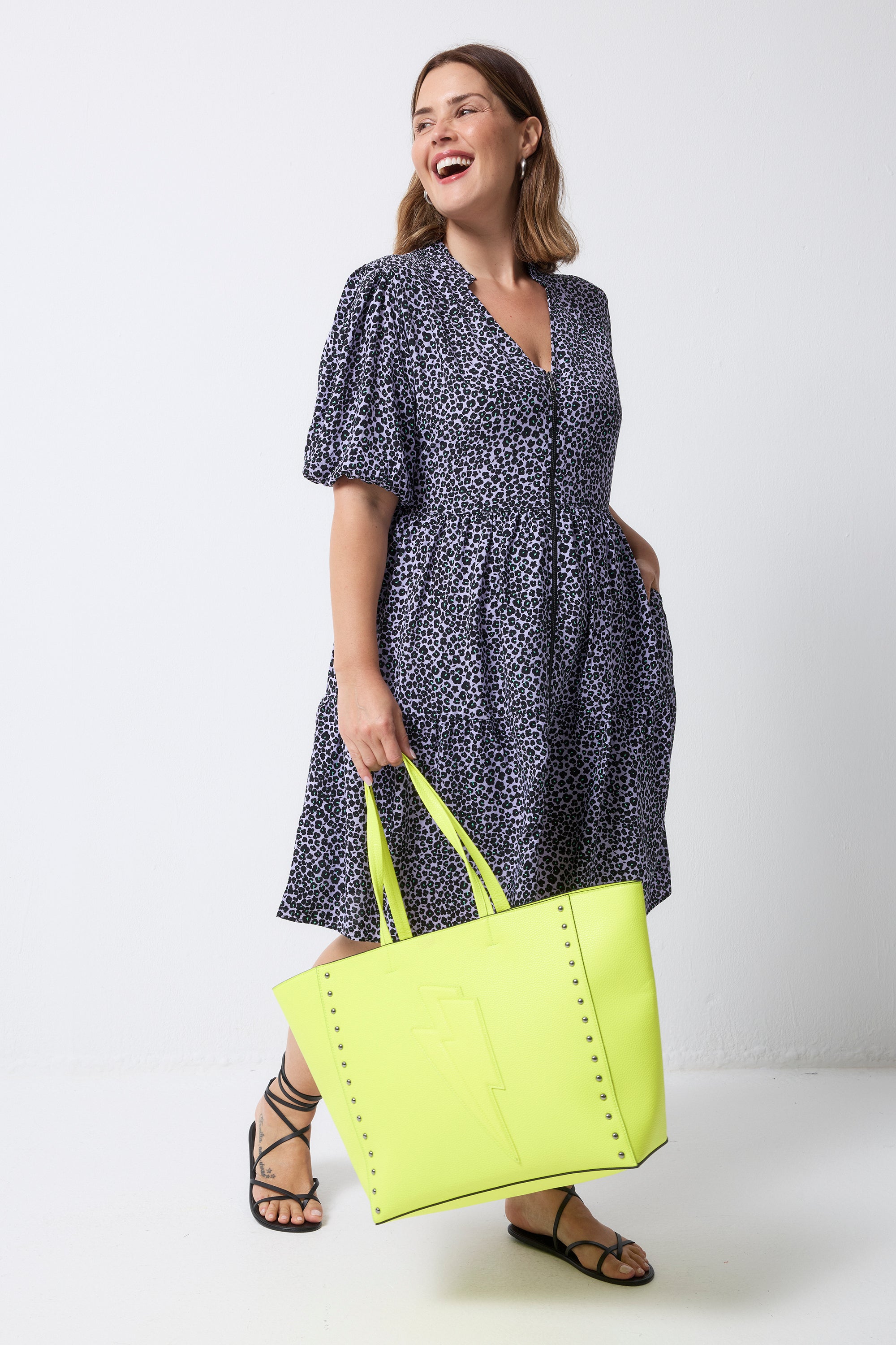 Scamp and Dude Lilac Mini Leopard Zip Detail Tiered Short Dress | Model with short brown hair is wearing a lilac leopard print short dress with a zip front detail. Worn with black sandals and a neon yellow tote bag/