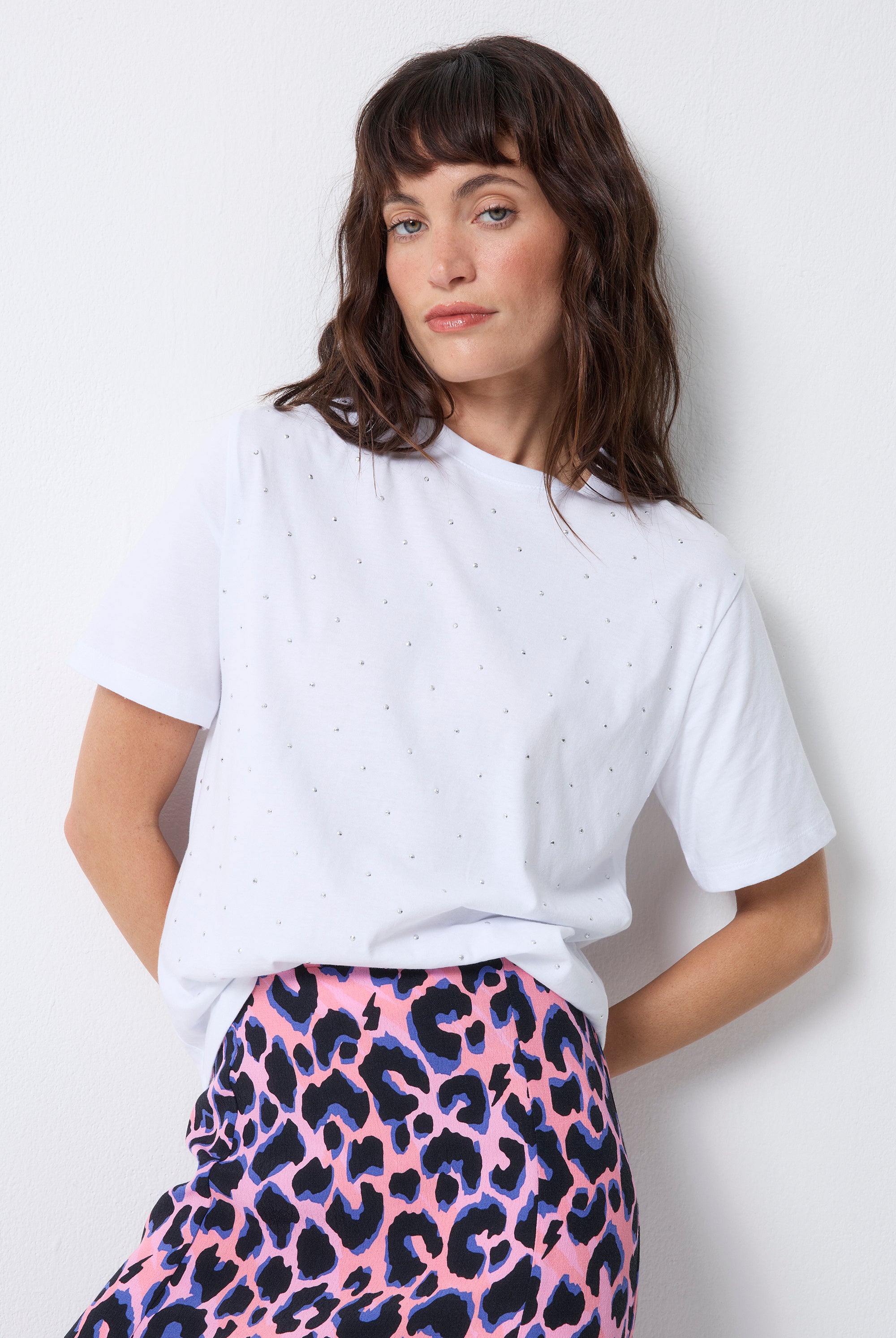 Scamp and Dude White Studded Relaxed Band T-Shirt | Model wearing short sleeve white t-shirt with stud detail, paired with a pink with blue and black leopard print skirt.