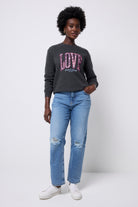 Scamp and Dude Dark Grey Love Cheetah Oversized Sweatshirt | Model wearing blue distressed jeans with a dark grey oversized sweatshirt. The sweatshirt has 'LOVE'  in a blue and white cheetah print across the front of the sweatshirt with pink embroidery.