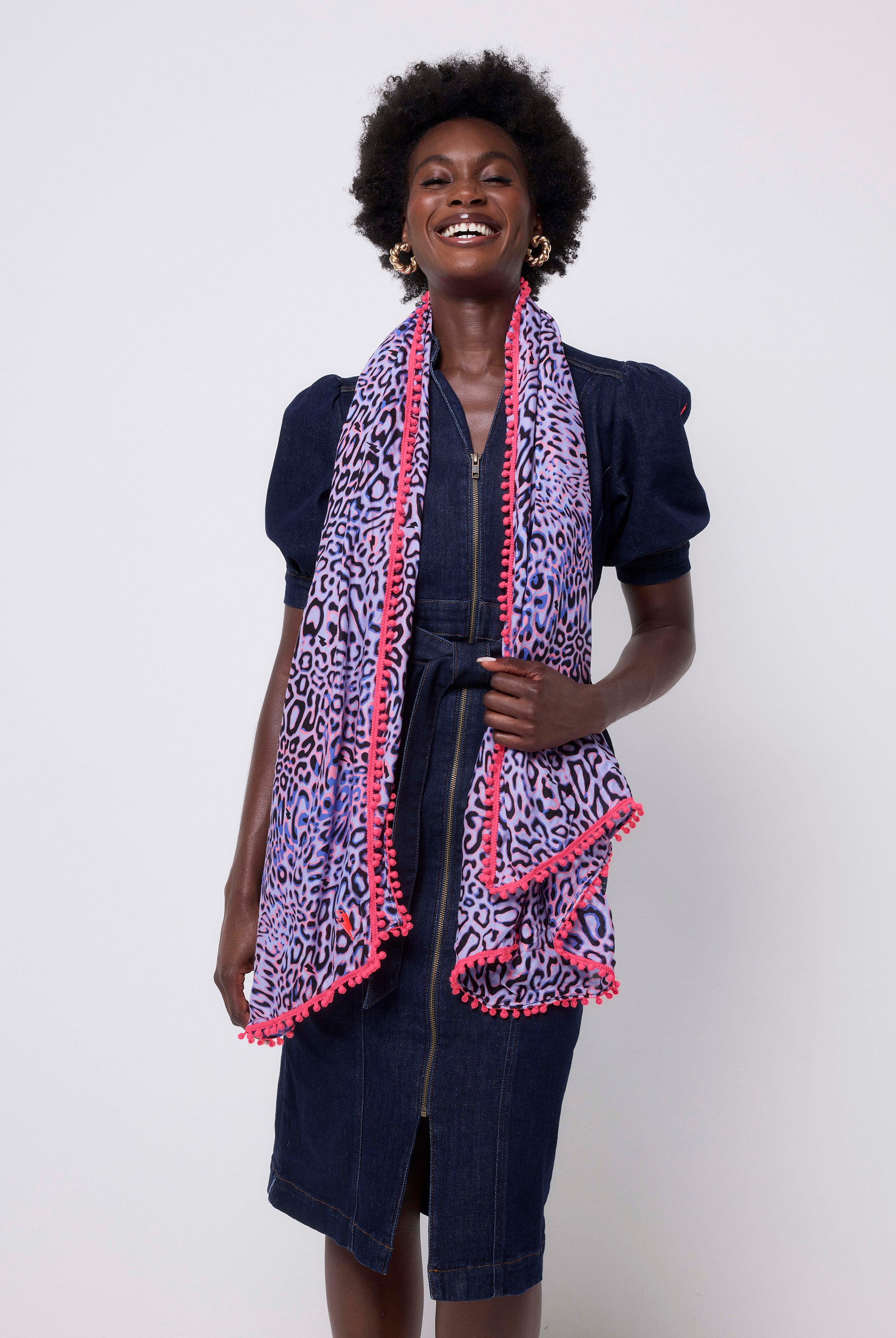 Scamp and Dude Lilac with Black and Pink Leopard Ray Super Scarf | Model wearing a dark blue denim dress with a lilac leopard ray print scarf with neon pink pom poms.