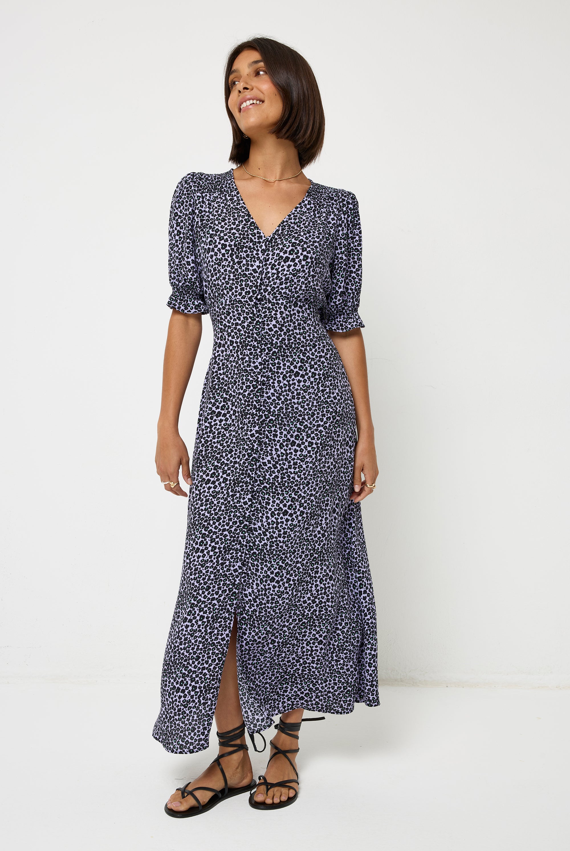 Scamp and Dude Lilac Mini Leopard Flute Sleeve Midi Tea Dress | Model with short dark hair wearing a lilac midi length tea dress with short flute sleeves and a button front detail. Worn with black strappy sandals and a gold necklace.