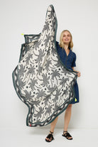 Scamp and Dude White with Black and Khaki Palm Spring Charity Super Scarf | Model wearing a short dark blue denim dress with black sandals, holding a white and khaki palm print super scarf.