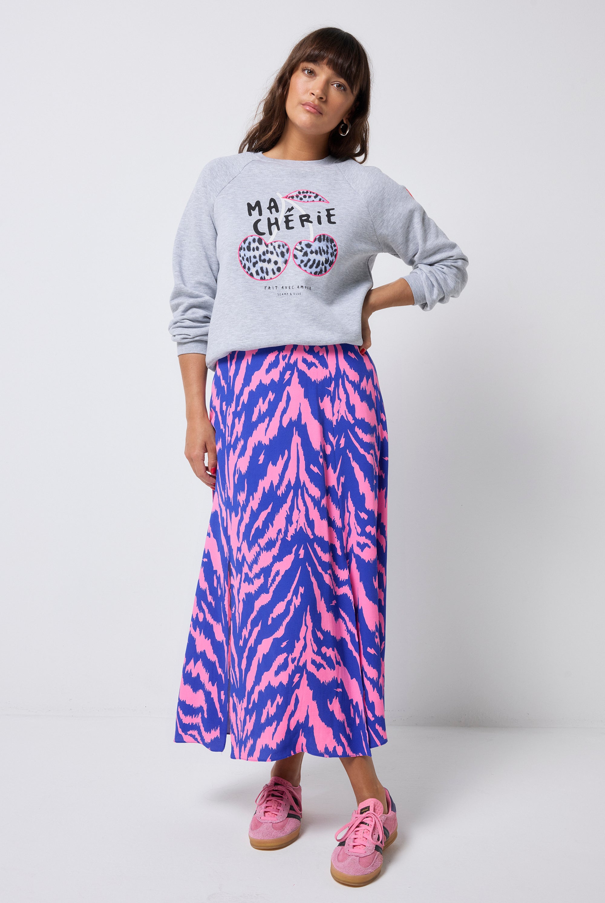 Scamp and Dude Light Grey Marl Ma Cherie Oversized Sweatshirt | Model wearing a grey oversized sweatshirt with a cherry applique. Worn with a pink and blue tiger print skirt and pink trainers.