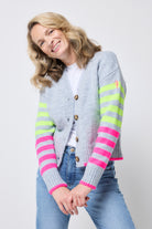 Scamp and Dude Grey with Neon Yellow and Neon Pink Stripe Cardigan | Model with blonde hair wearing a pair of blue jeans with a white t-shirt and grey cardigan. The grey cardigan has neon yellow and pink stripes on the sleeves.