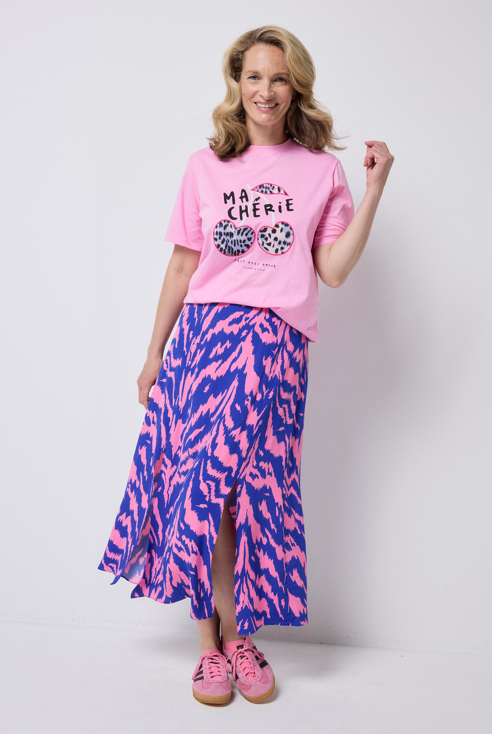 Scamp and Dude Pink Ma Cherie Graphic Print Band T-Shirt | Model wearing a pink graphic t-shirt with ma cherie slogan and cherry applique print. Wone with a pink and blue zebra print skirt and pink trainers.
