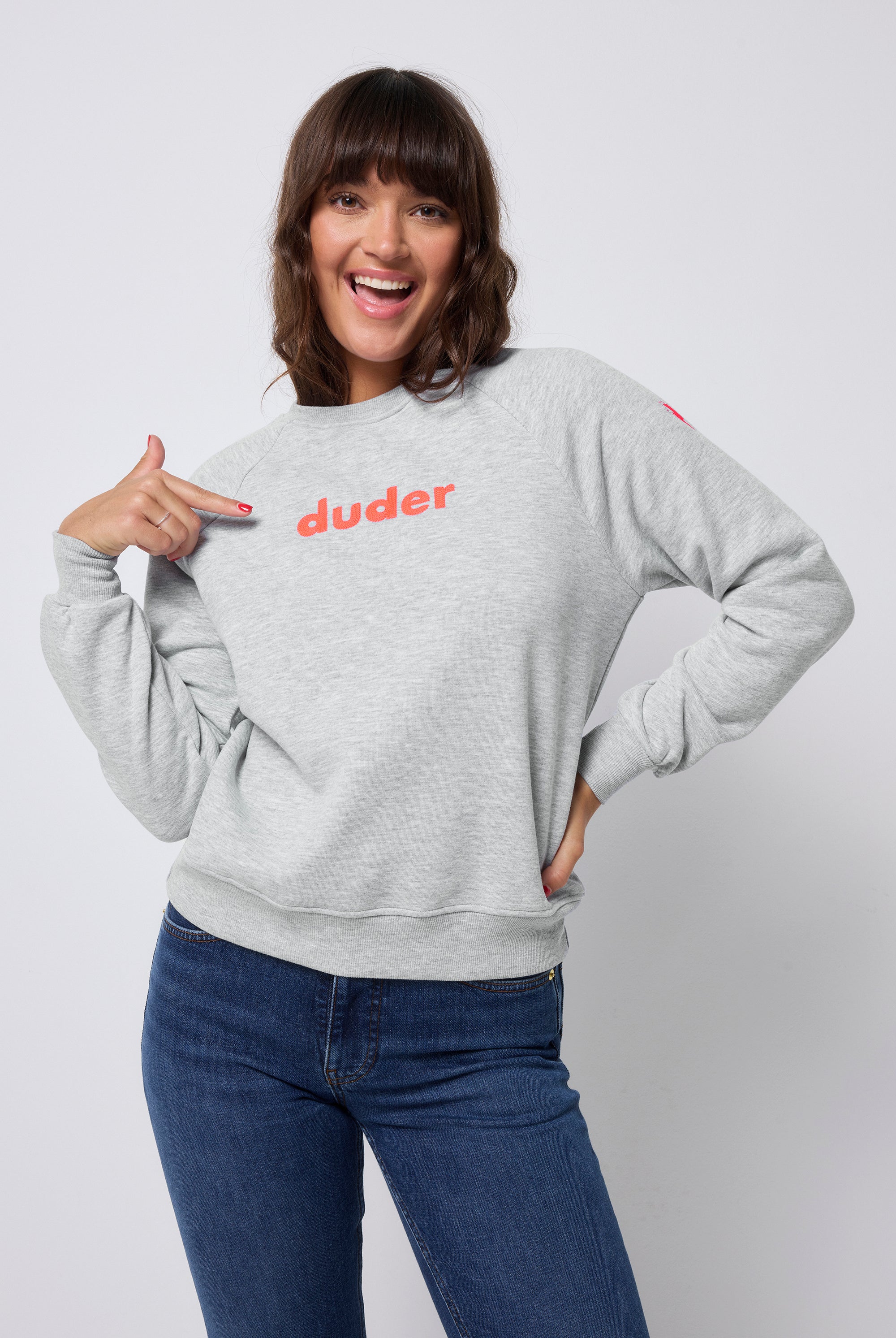 Scamp and Dude Grey Marl Duder Embroidery Oversized Sweatshirt | Model wearing a grey marl crew neck sweatshirt with neon coral 'duder' embroidery on the chest. Worn with dark blue jeans.