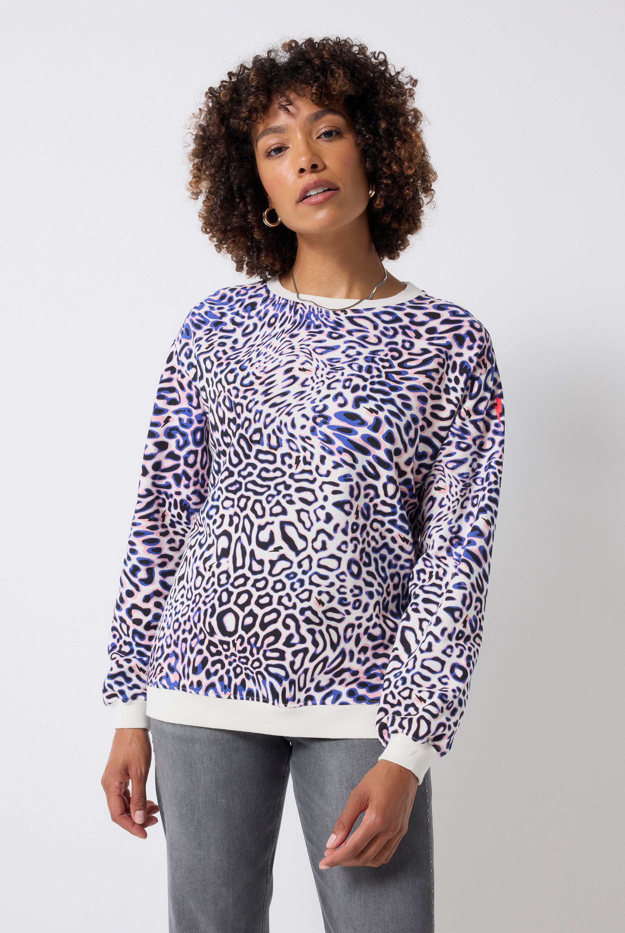 Scamp and Dude Ivory with Blue and Pink Leopard Ray Oversized Sweatshirt | Model wearing a crew neck sweatshirt with blue and pink leopard ray print. Worn with grey studded jeans.