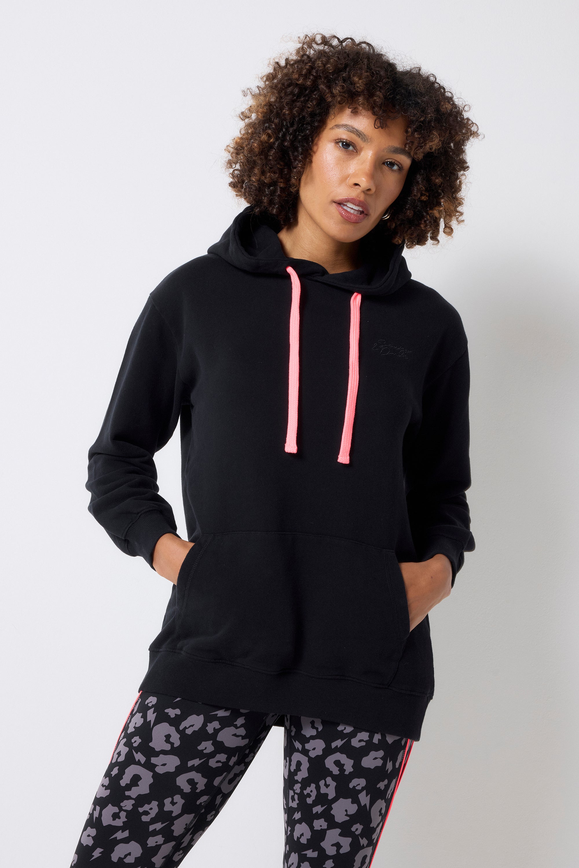 Scamp and Dude Black Longline Hoodie | Model wearing a pair of grey leopard print leggings with a black longline hoodie featuring neon coral drawstrings.