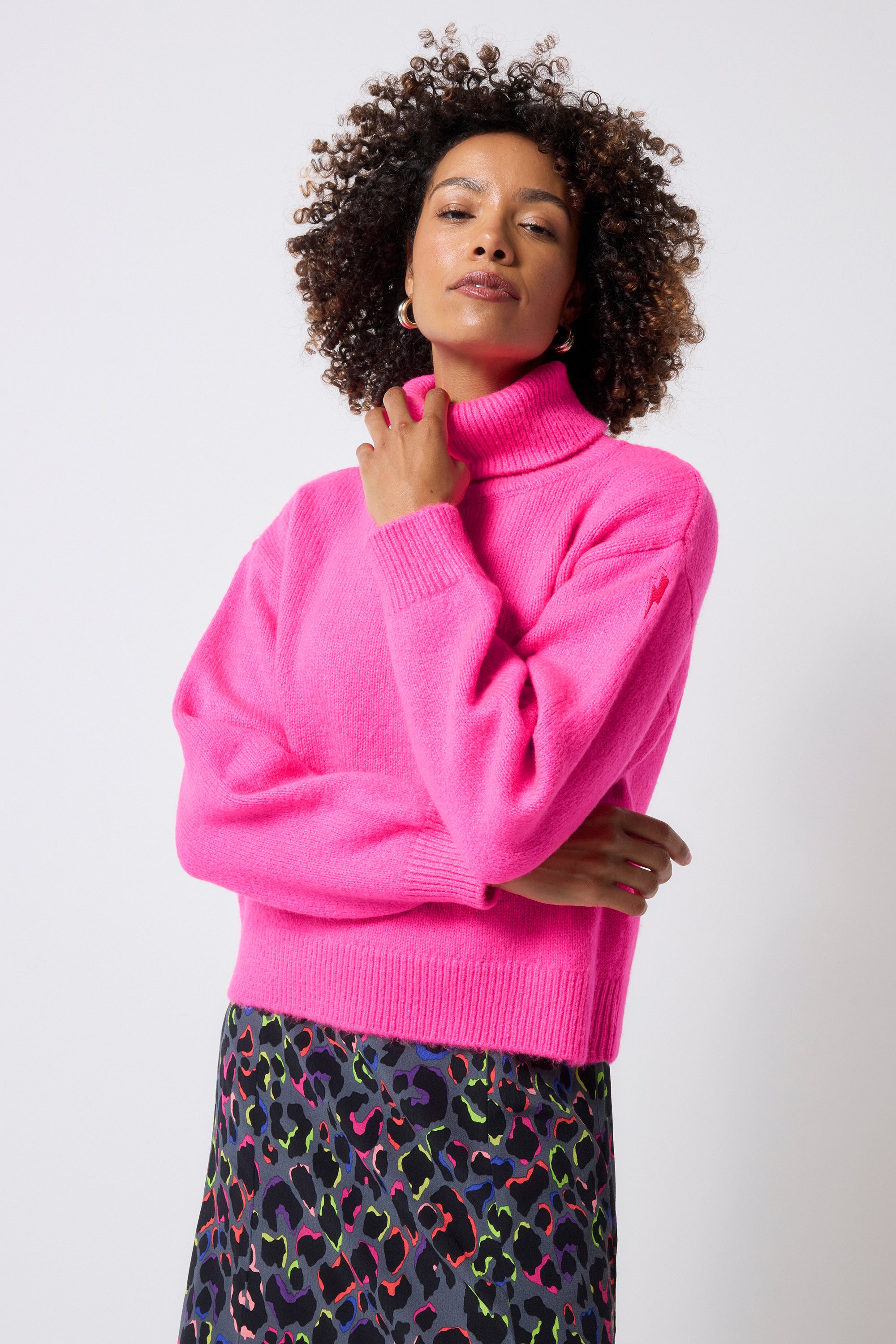 Scamp and Dude Pink Turtleneck Knitted Jumper | Model wearing a pink turtleneck jumper with a grey rainbow leopard print midi skirt.