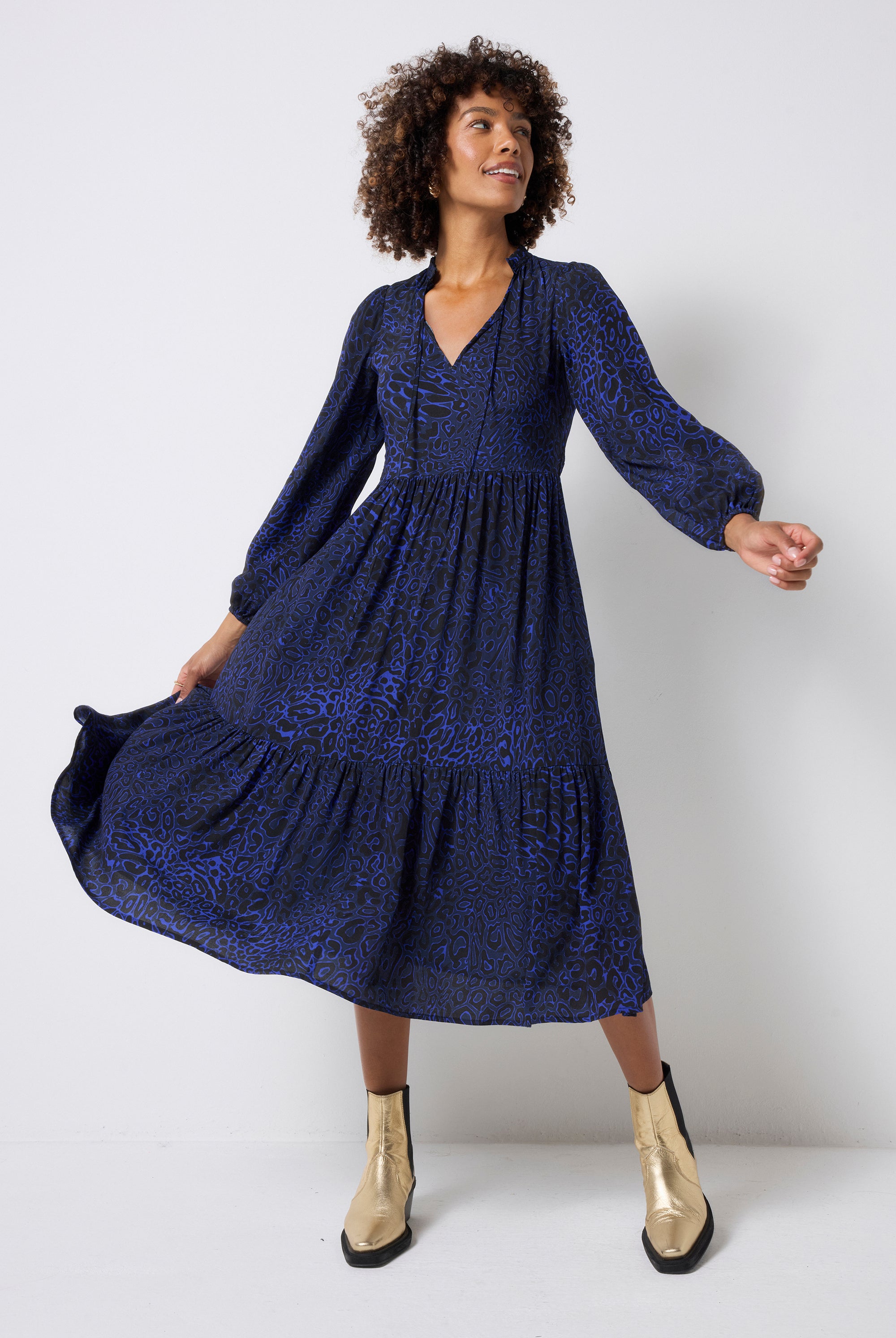 Scamp and Dude Navy Leopard Ray Blouson Sleeve Tie Front Midi Dress | Model wearing a long sleeve navy leopard ray print dress with tie front detail and gold boots.