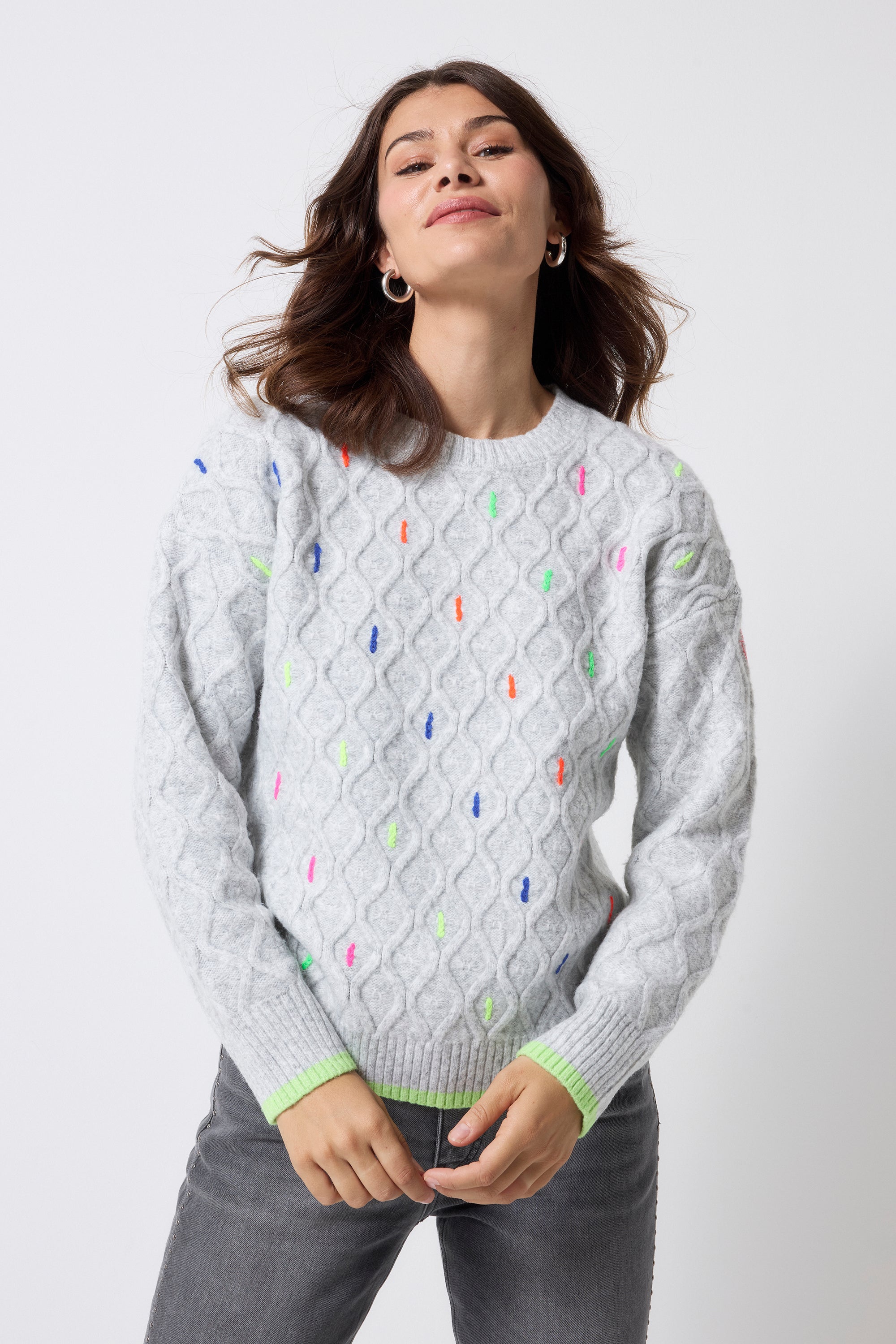 Scamp and Dude Grey with Neon Rainbow Fleck Cable Knit Jumper | Model wearing a pair of grey studded jeans with a grey cable knit jumper that has neon rainbow flecks.