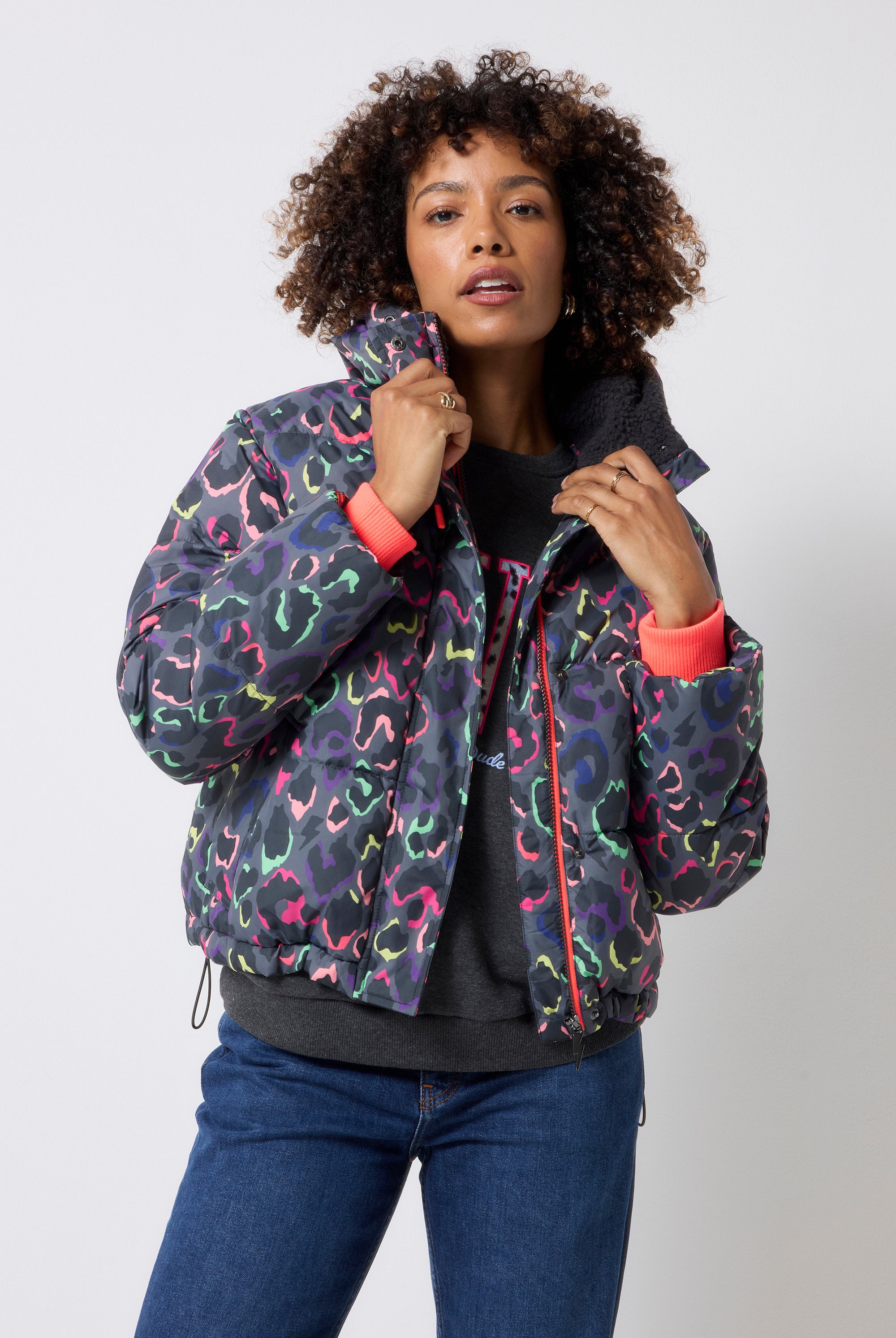 Scamp and Dude Grey with Rainbow Shadow Leopard Short Puffer Coat | Model wearing blue jeans with a dark grey love sweatshirt and a grey rainbow leopard puffer coat.