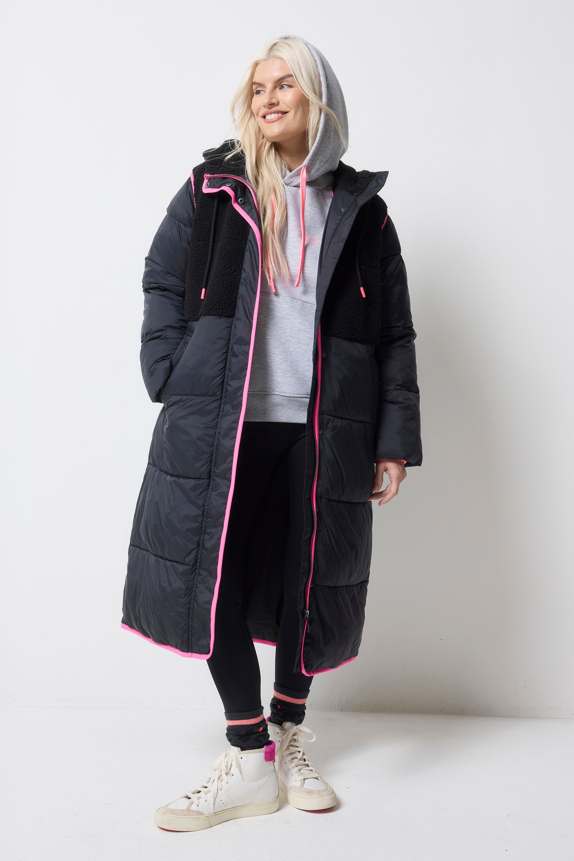 Scamp and Dude Black Puffer Coat | Model wearing a pair of black leggings with a light grey hoodie and black puffer coat featuring neon pink details.