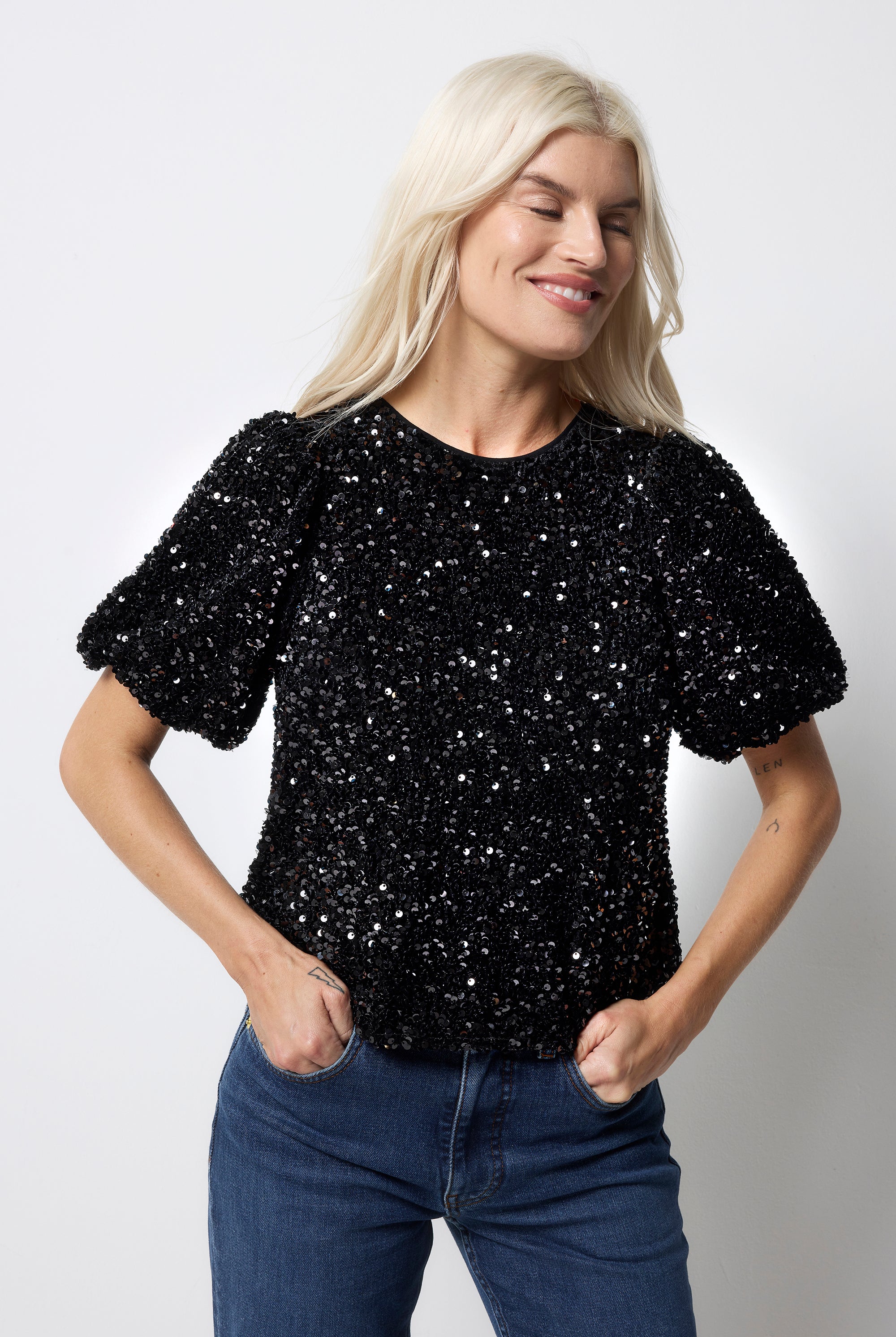 Scamp and Dude Black Sequin Tie Back Puff Sleeve Velvet Blouse | Model wearing a black sequin top with a tie back detail worn with blue jeans.