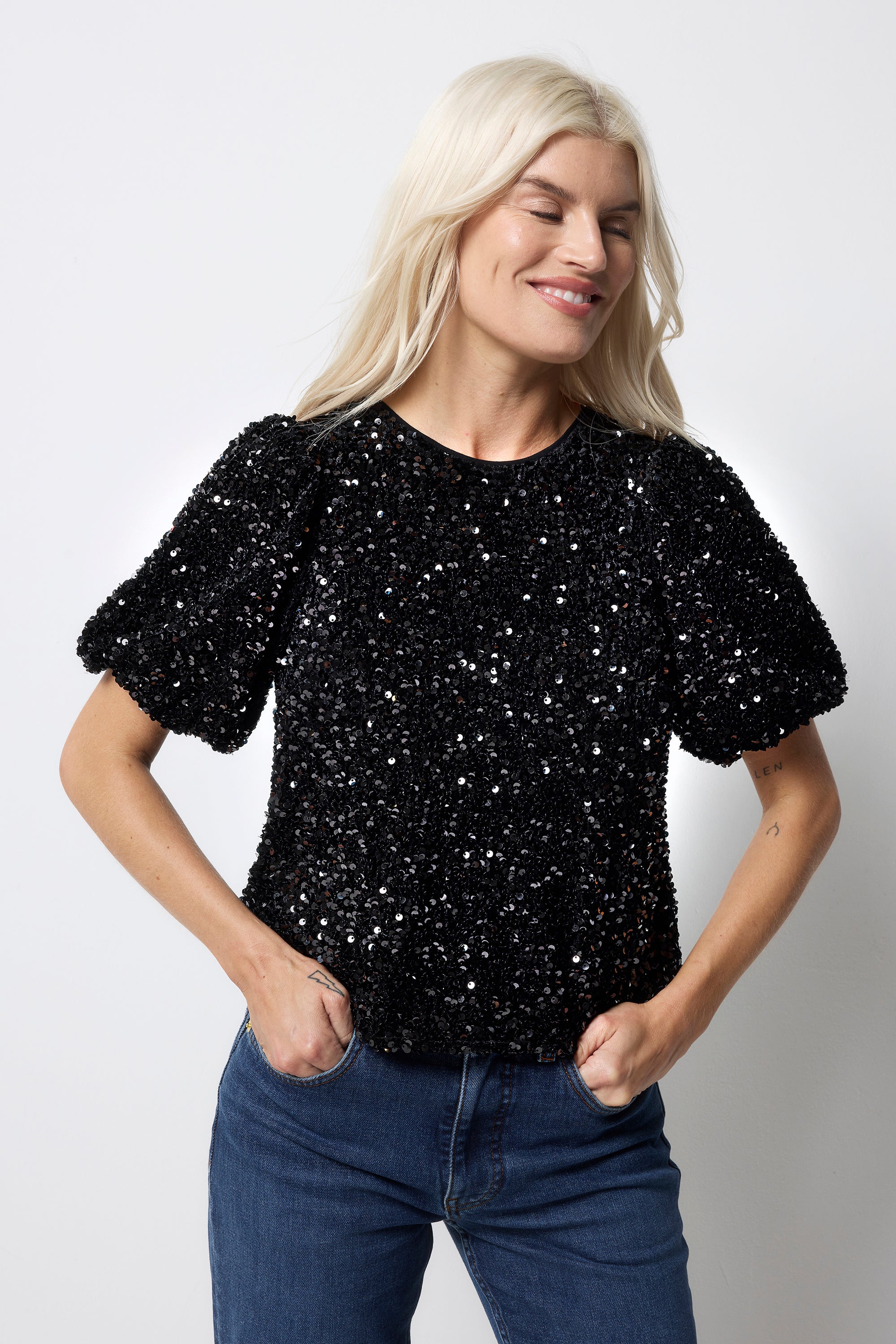 Scamp and Dude Black Sequin Tie Back Puff Sleeve Velvet Blouse | Model wearing a black sequin top with a tie back detail worn with blue jeans.