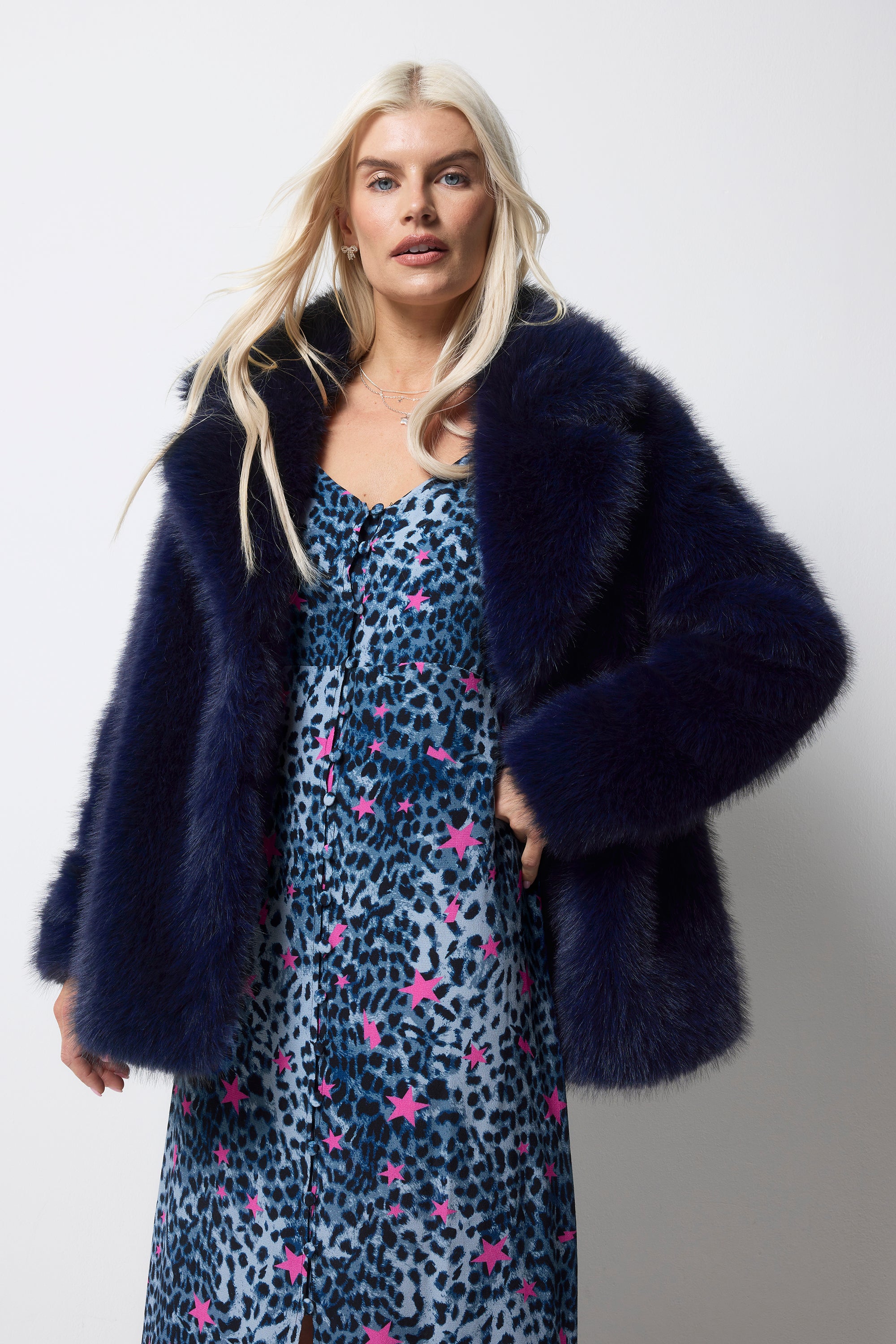 Scamp and Dude Midnight Blue Faux Fur Coat | Model wearing a navy cheetah dress with pink stars. Worn with a midnight blue faux fur coat over the top.