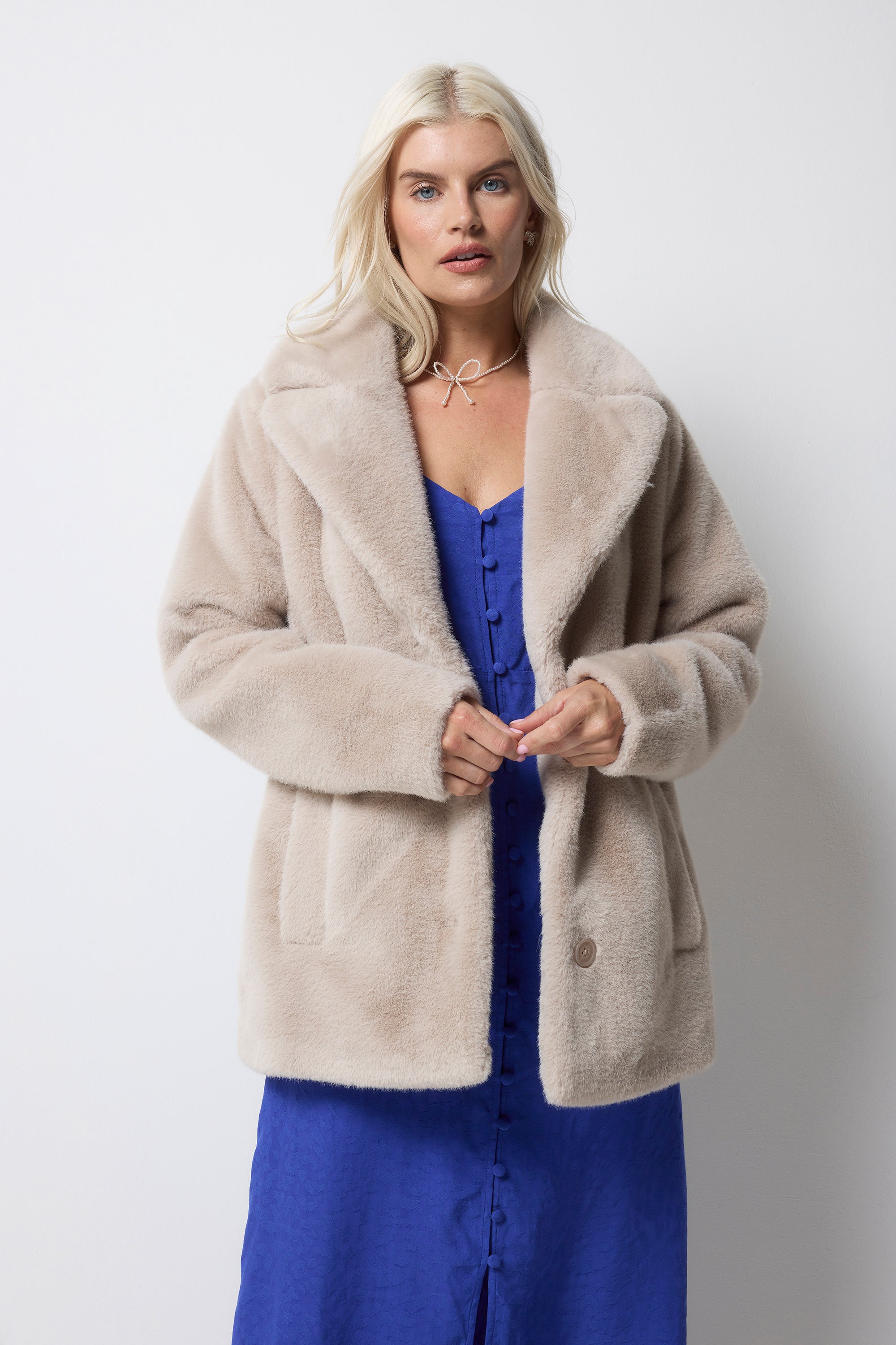 Scamp and Dude Cream Faux Fur Coat | Model wearing a blue tea dress with a cream fur jacket and silver jewellery.