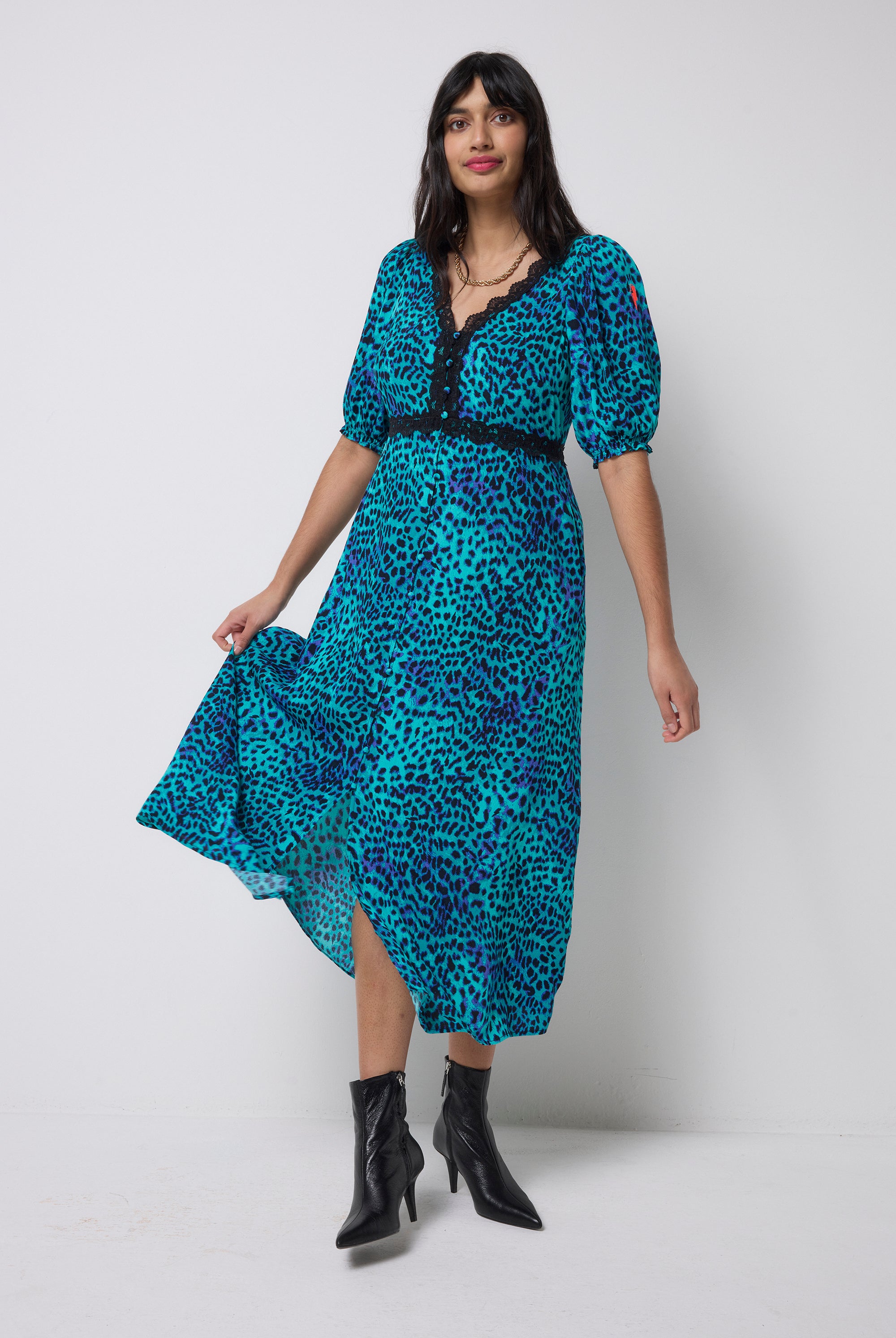 Scamp and Dude Turquoise with Blue Cheetah Lace Trim Puff Sleeve Midi Tea Dress | Model wearing a turquoise cheetah print dress with lace trim detail and black heeled boots.