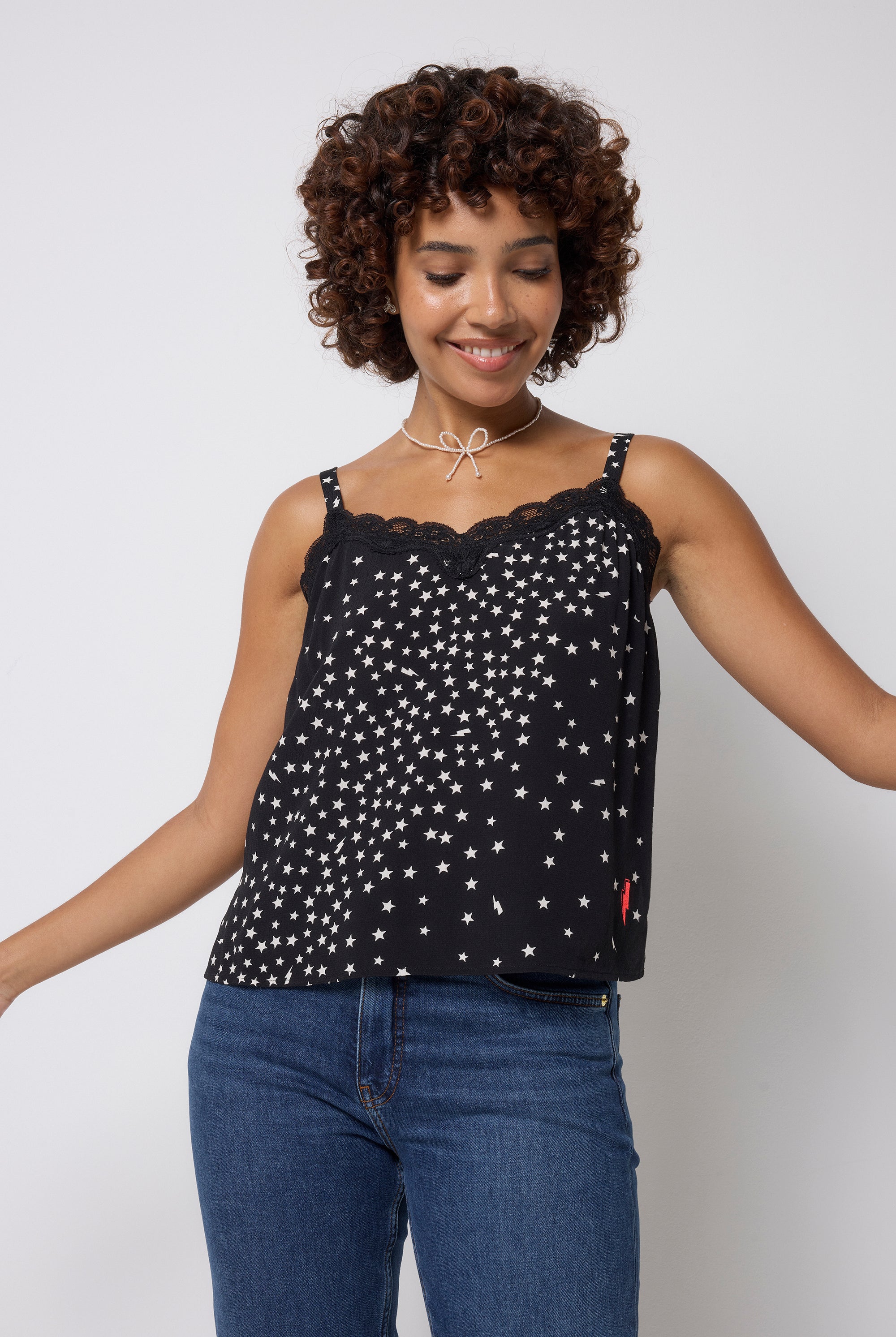 Scamp and Dude Black with White Star Cluster Lace Trim Cami Top | Model wearing a black cami top with lace trim and white star print. Worn with dark blue jeans.