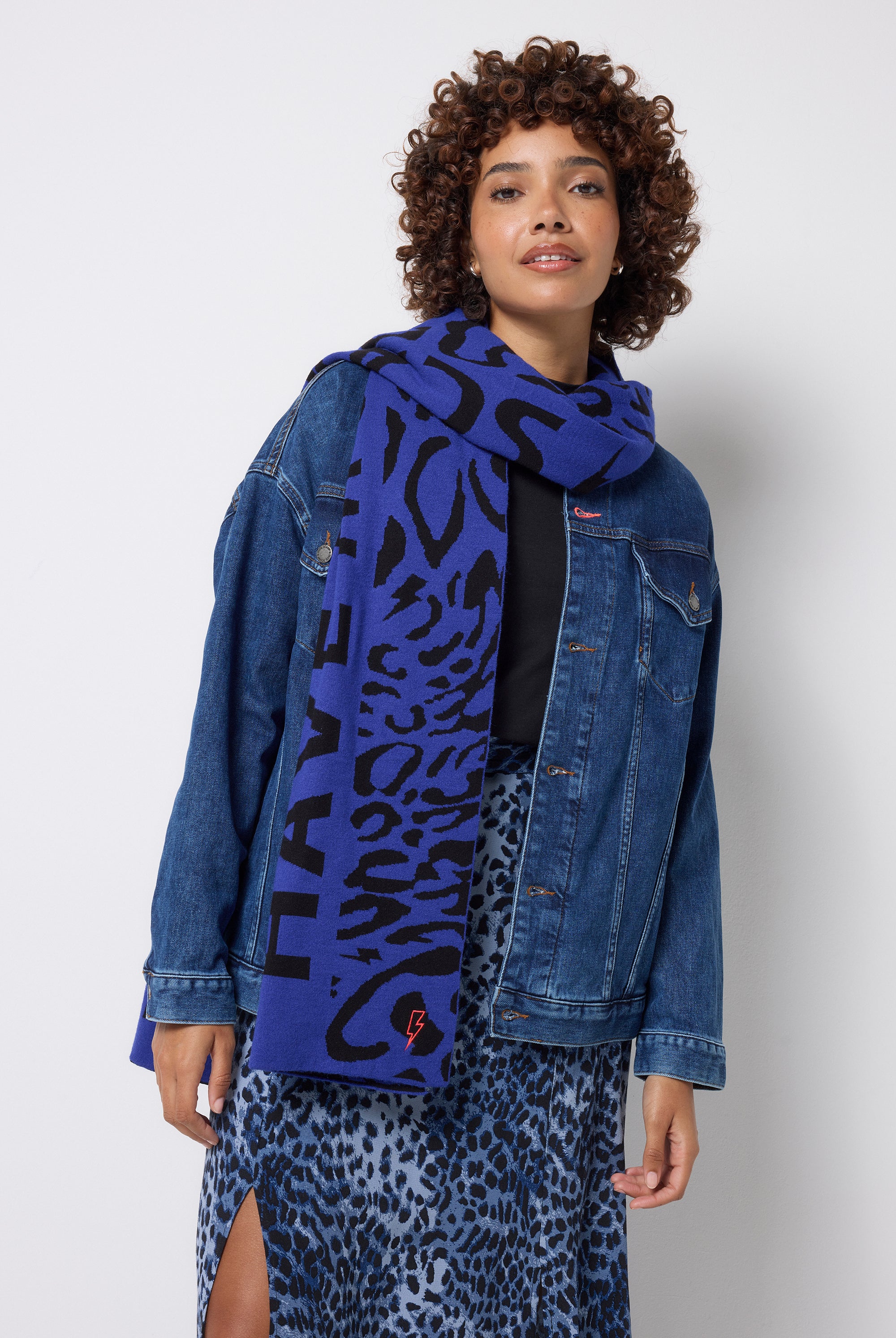 Scamp and Dude Navy with Black Slogan Jacquard Scarf | Model wearing a navy cheetah print skirt, black t-shirt and oversized denim jacket with a blue and black printed scarf.