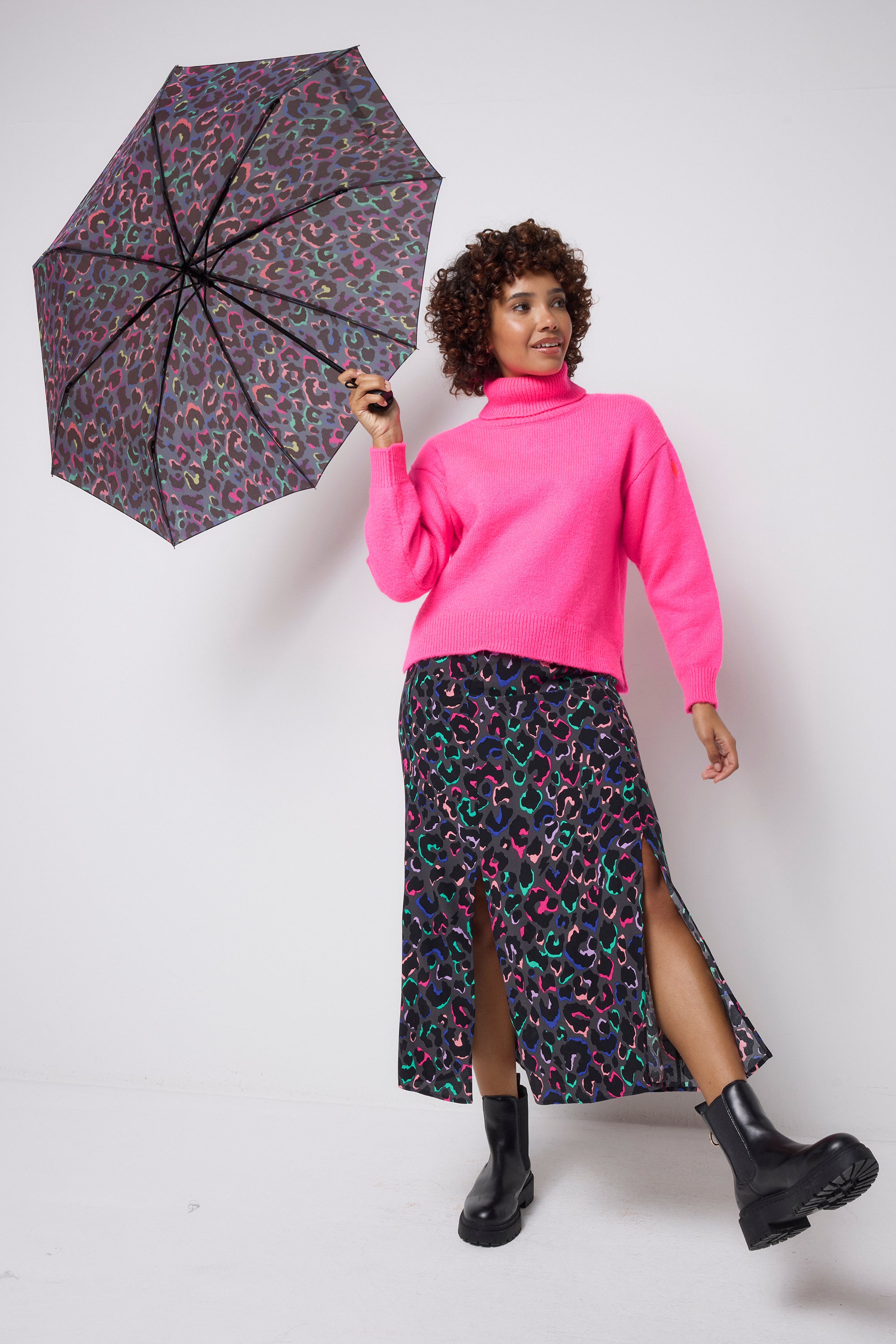 Scamp and Dude Grey with Rainbow Shadow Leopard Umbrella | Model wearing a rainbow leopard print skirt with a pink turtleneck knitted jumper and black boots. Model is holding a rainbow leopard print umbrella.