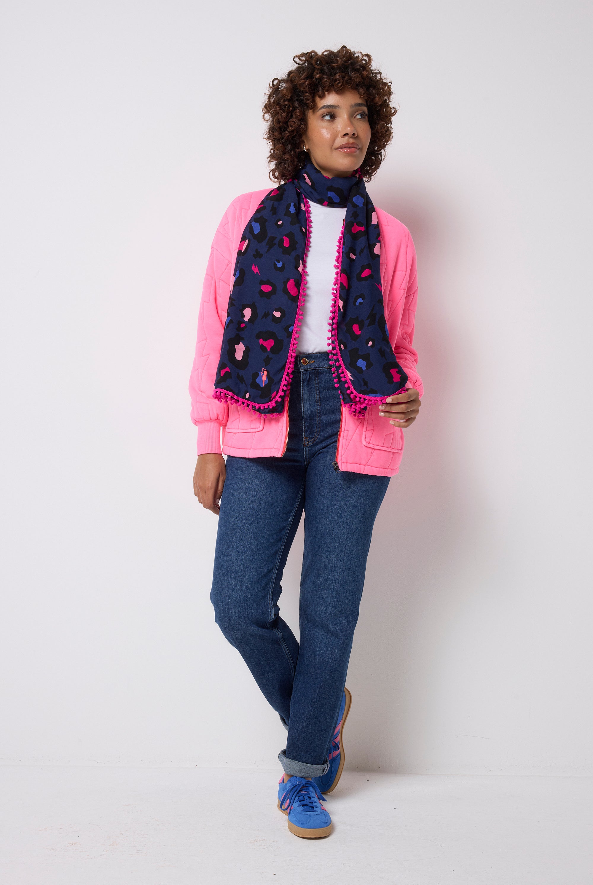 Scamp and Dude Navy with Pink Snow Leopard Charity Super Scarf | Model wearing a navy snow leopard print super scarf with a pink trim. Worn with pair of dark blue jeans, a white t-shirt and pink bomber jacket.