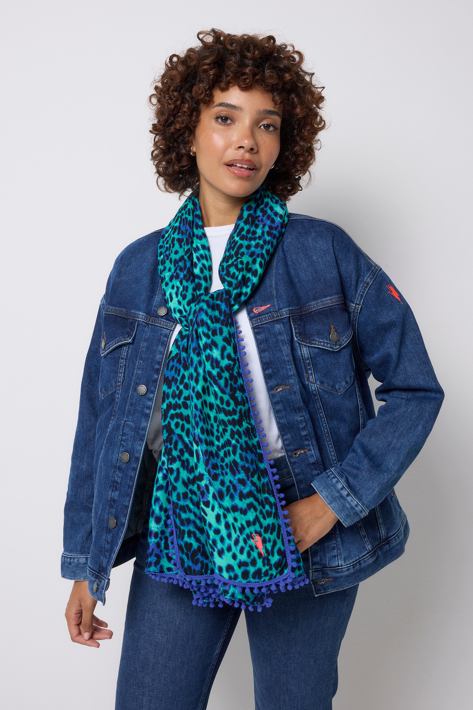 Scamp & Dude Turquoise with Blue Cheetah Charity Super Scarf | Model wearing a blue denim jacket and a turquoise cheetah print scarf against a white background.