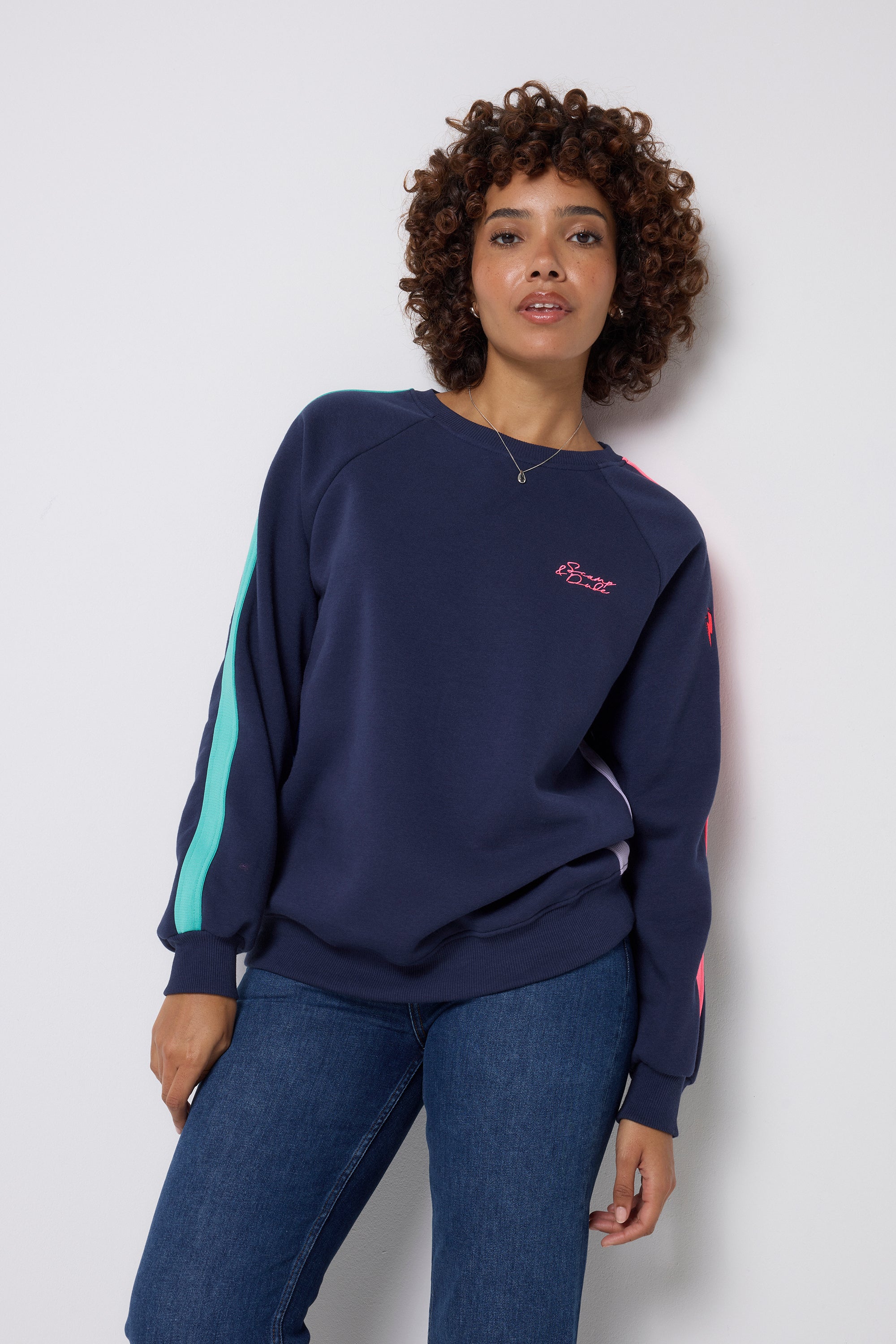 Scamp and Dude Navy with Rainbow Colourblock Sweatshirt | Model wearing dark navy jumper with multi coloured colourblock stripes down the side and sleeves. Worn with dark blue jeans.