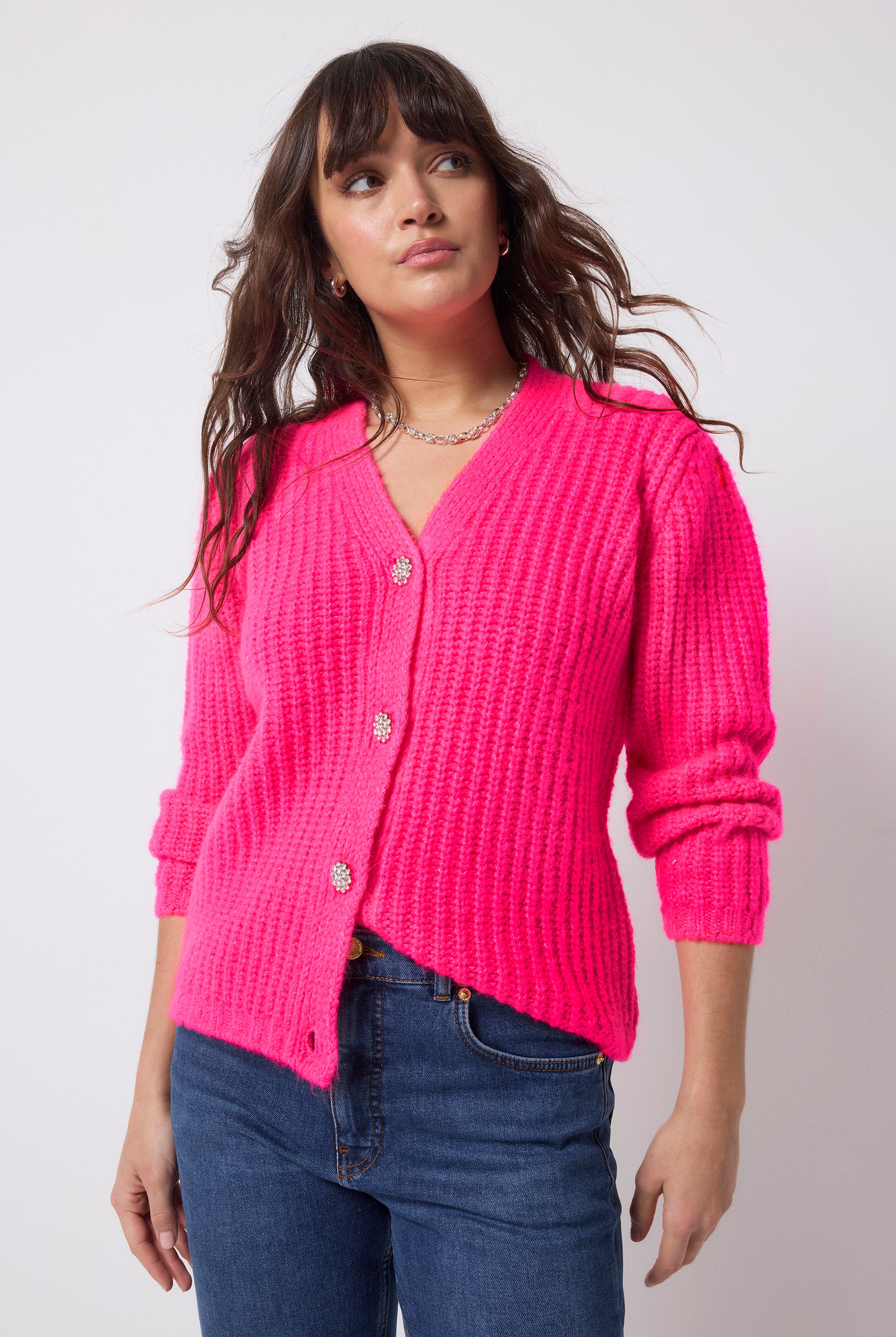 Scamp and Dude Neon Pink Button Through Cardigan | Model wearing a pair of dark blue jeans with a neon pink cardigan that has diamante button detail.