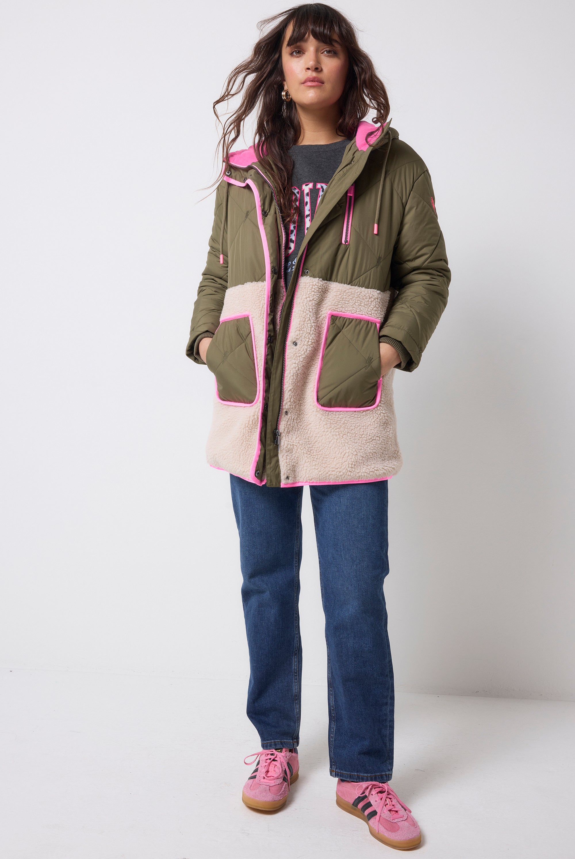 Scamp and Dude Khaki and Pink Quilted Borg Hooded Coat | Model wearing a pair of dark blue jeans with a grey sweatshirt and khaki borg coat which features pink details.