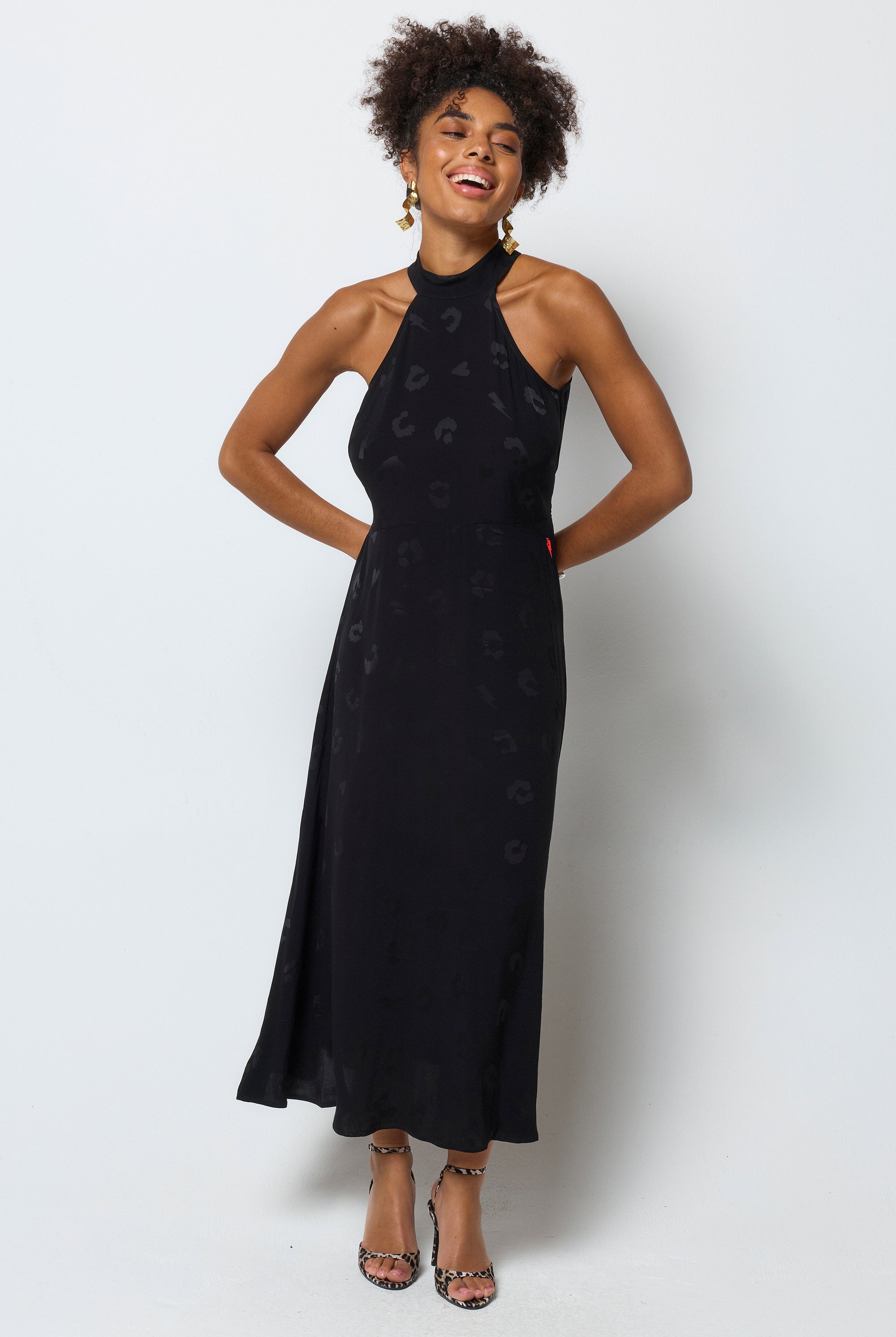 Scamp & Dude Black Jacquard Halter Midi Dress | Model wears a black halterneck dress in a leopard jacquard print. Worn with printed heels and gold jewellery.